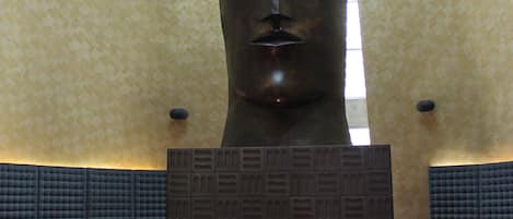 A restaurant with a large sculpture in the center, red upholstered chairs, and a patterned wall.