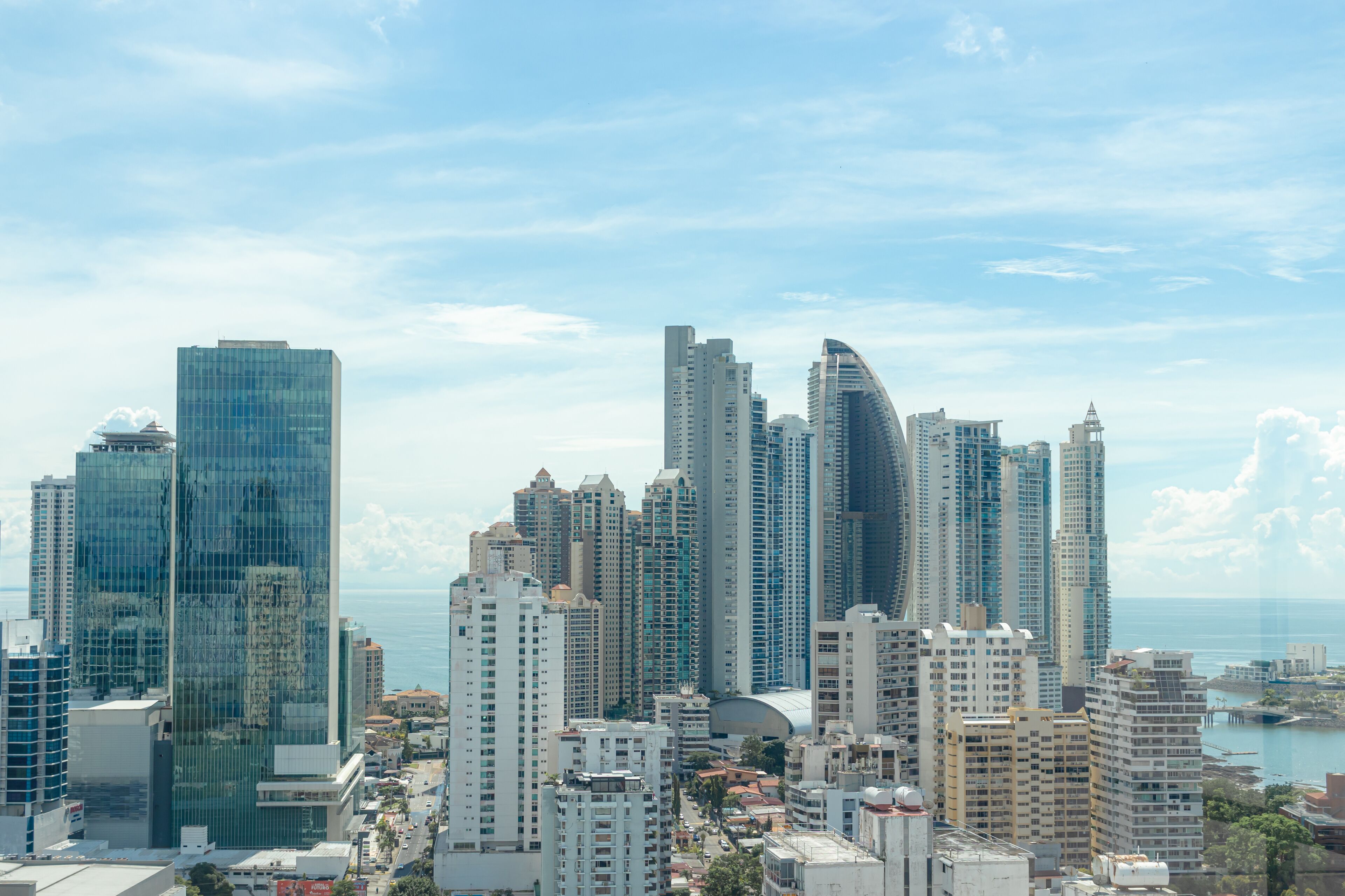 A cityscape with high-rise buildings, including a distinctive curved skyscraper, and a body of water in the background.