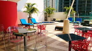 Un espace de détente aménagé sur le toit, avec des tables et des chaises en verre transparent, une piscine et des plantes en pot.