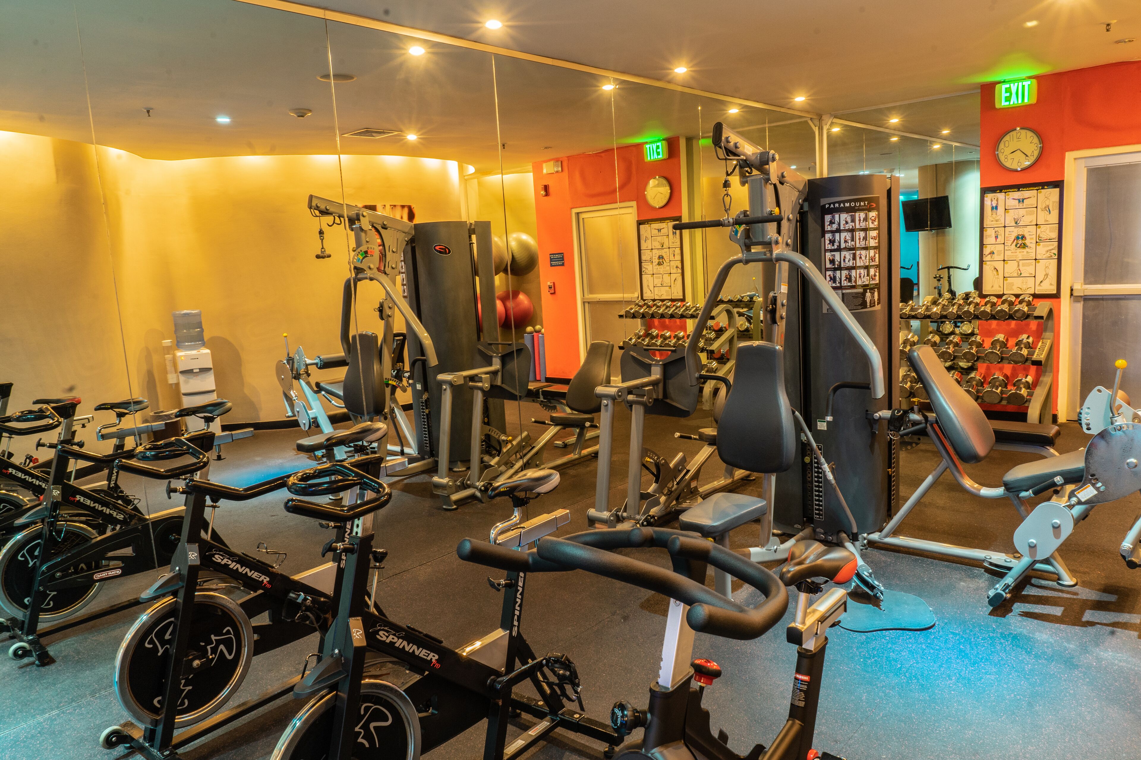 Ett gym med olika typer av träningsutrustning, inklusive motionscyklar, styrketräningsmaskiner och lösa vikter.