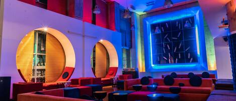 A modern lounge area with circular wooden accents, red seating, and a blue-lit wall.