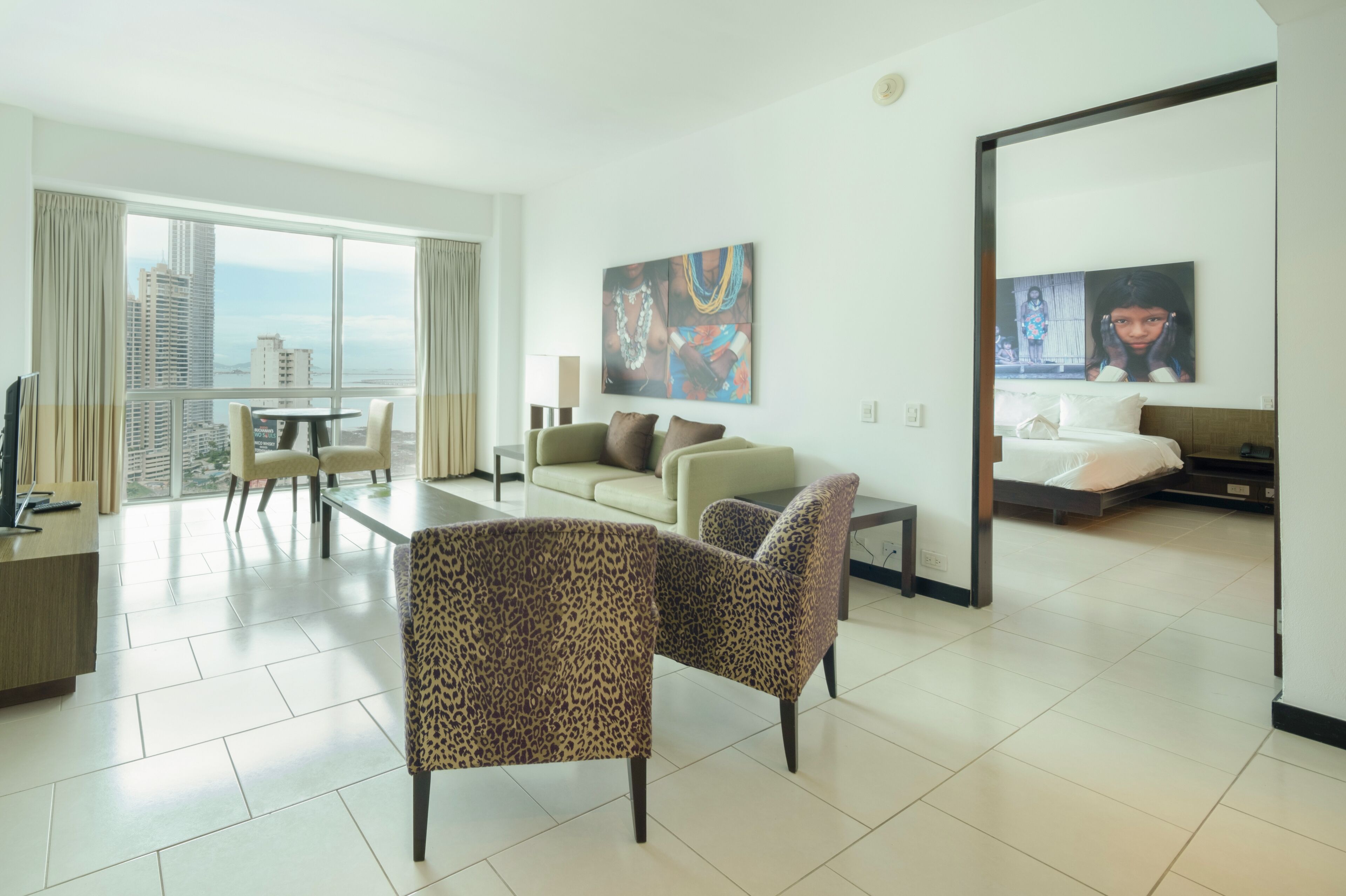 A modern hotel room with a balcony, a sofa, a dining table, and a bed.