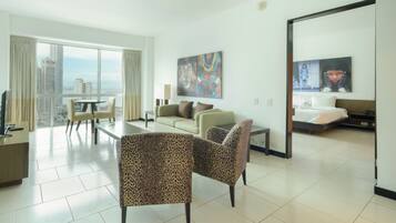 A modern hotel room with a balcony, a sofa, a dining table, and a bed.