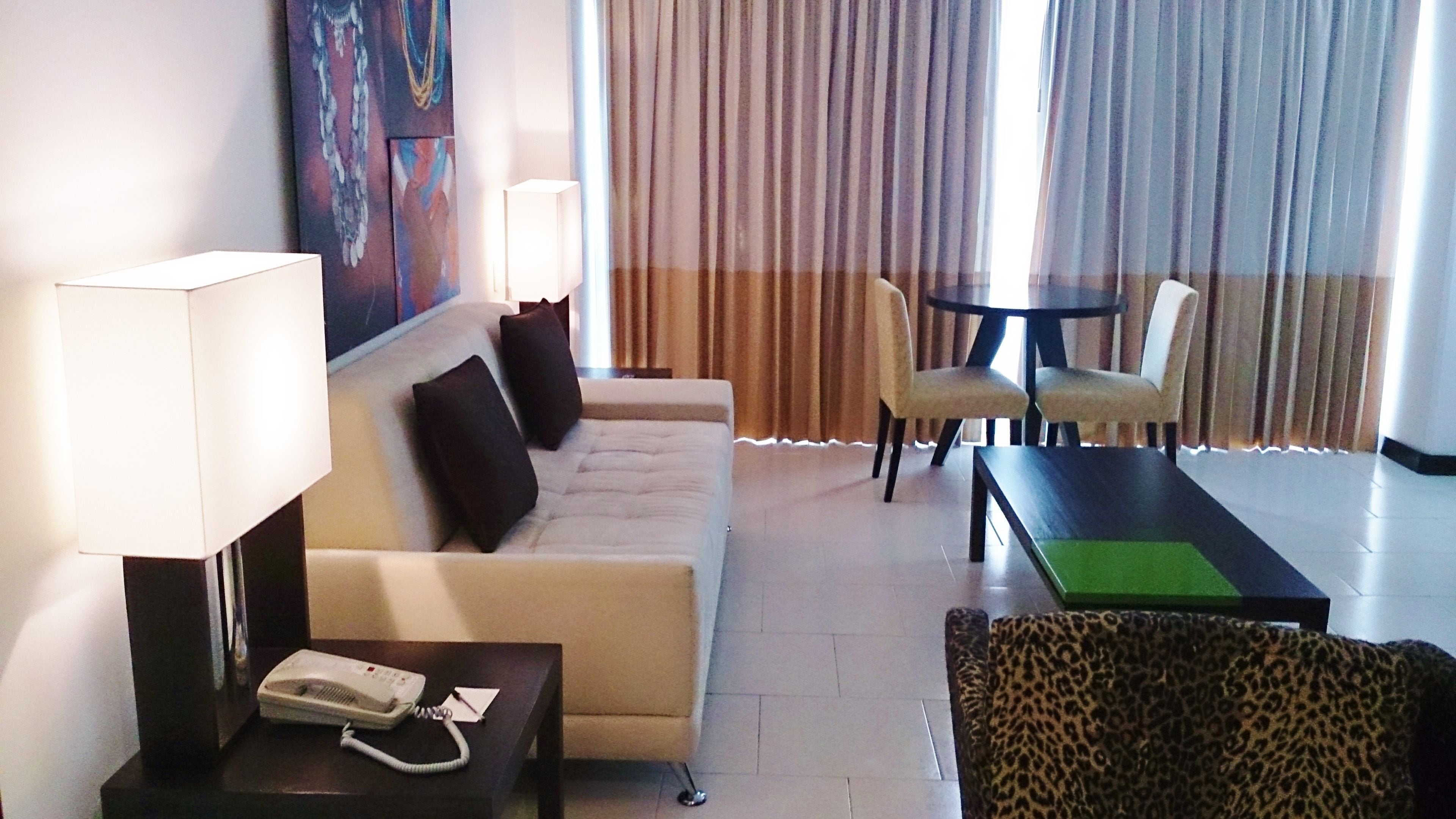 A hotel room with a sofa, two chairs, a table, a lamp, and a telephone on a side table.