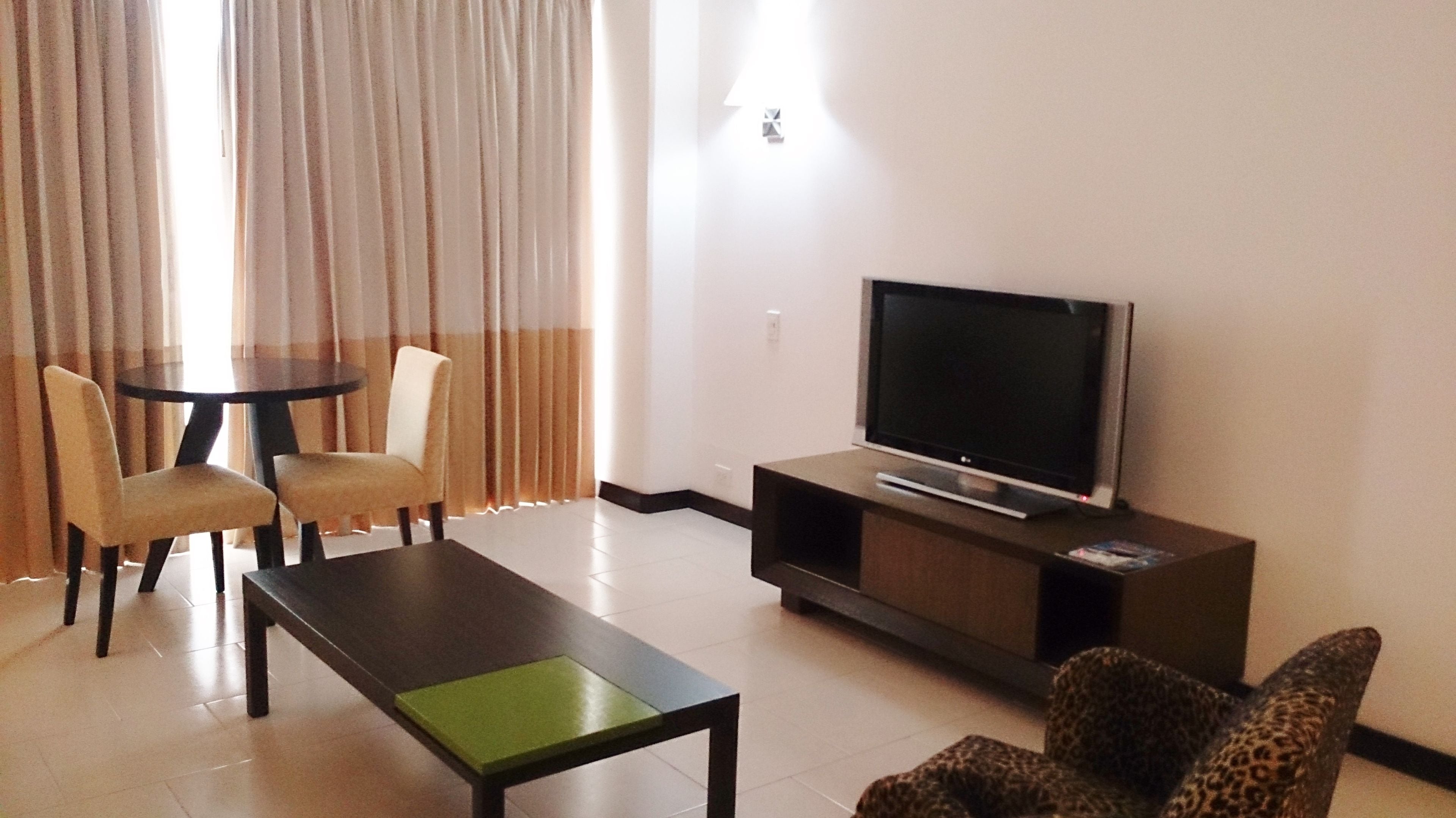 Una sala de estar con una televisión de pantalla plana sobre un soporte, una mesa de centro, dos sillones y un sofá.
