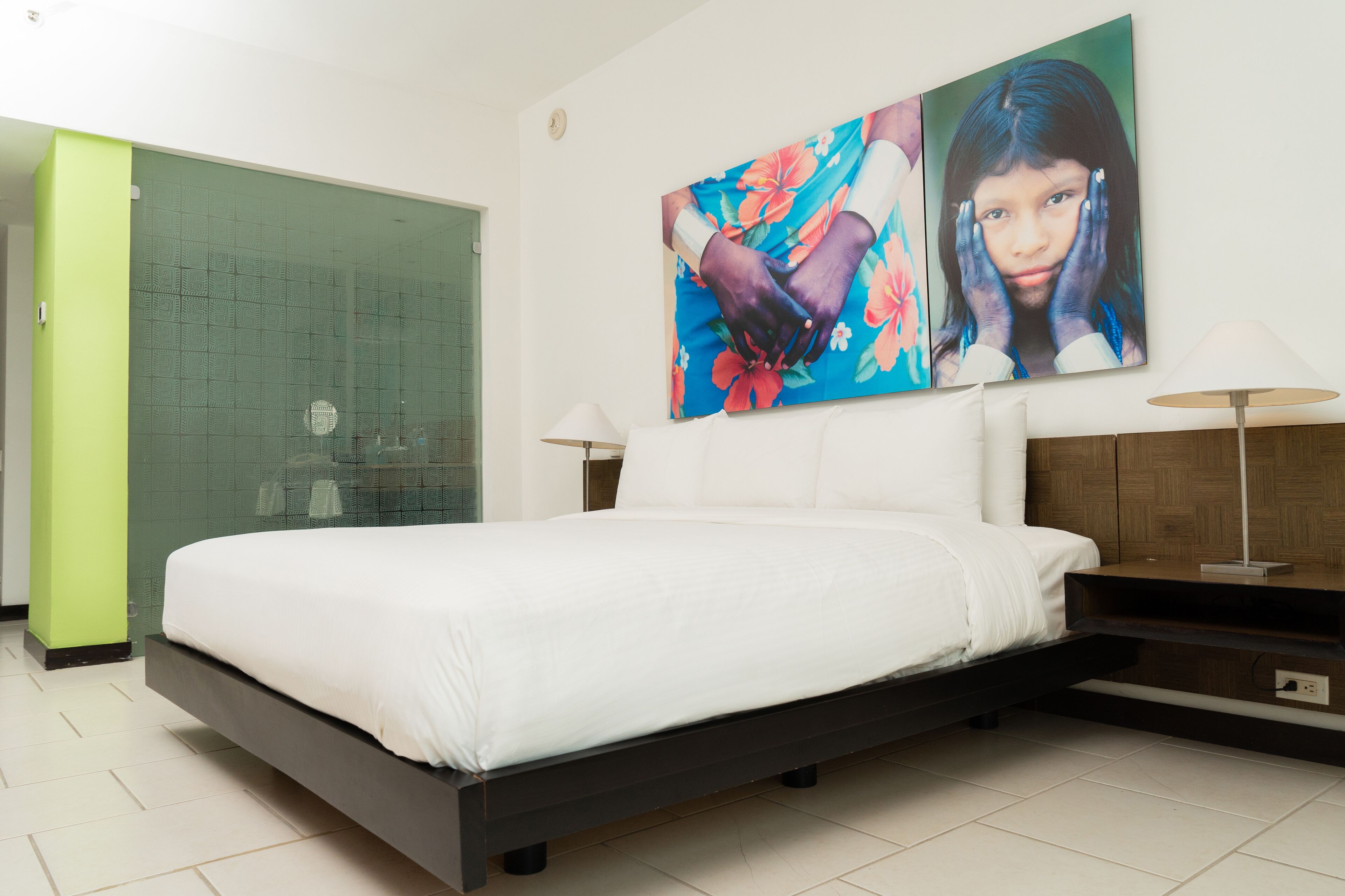 A modern hotel room with a large bed, a glass shower enclosure, and a large floral artwork on the wall.