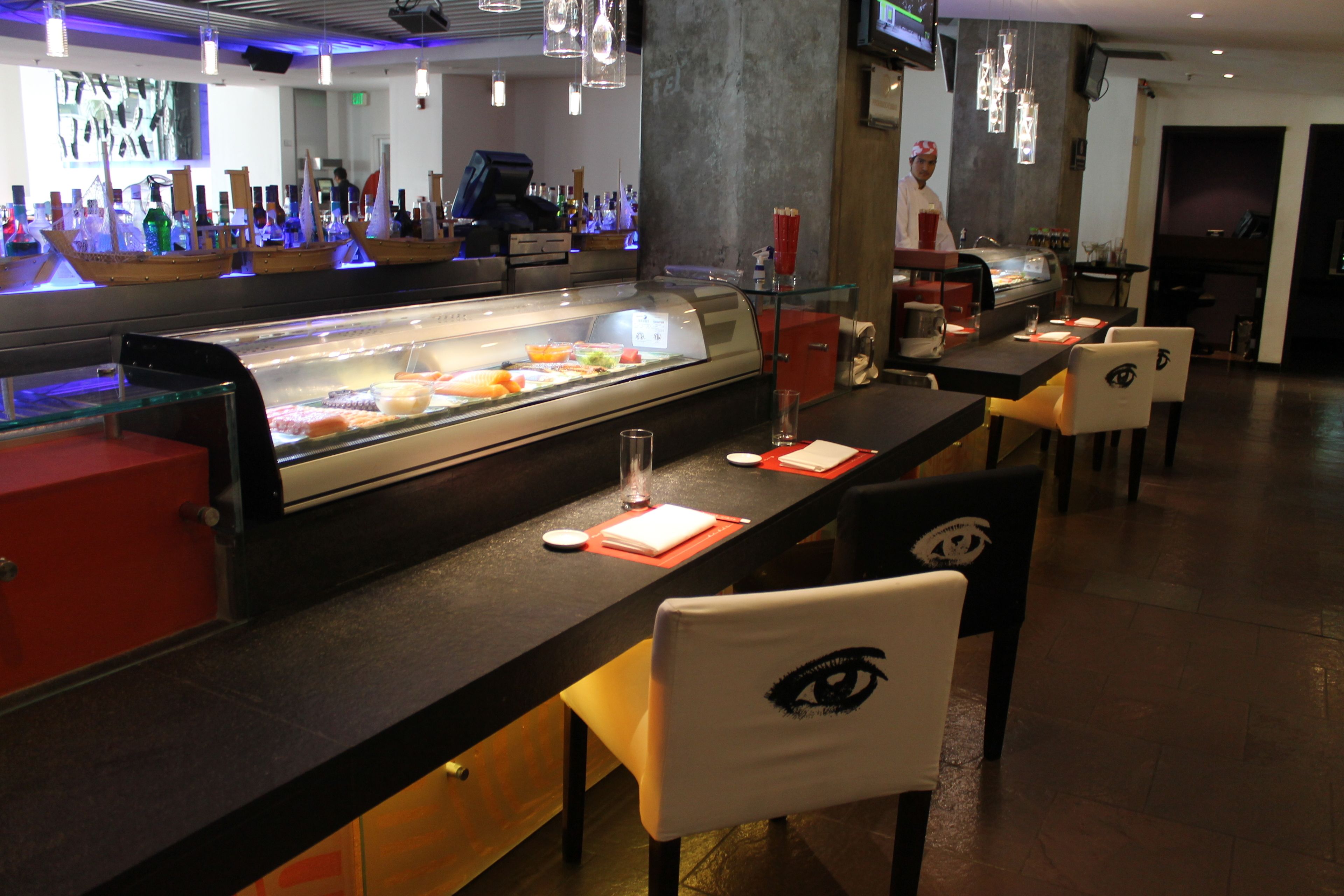 A bar area with a display case of food items, bar stools, and a bartender.