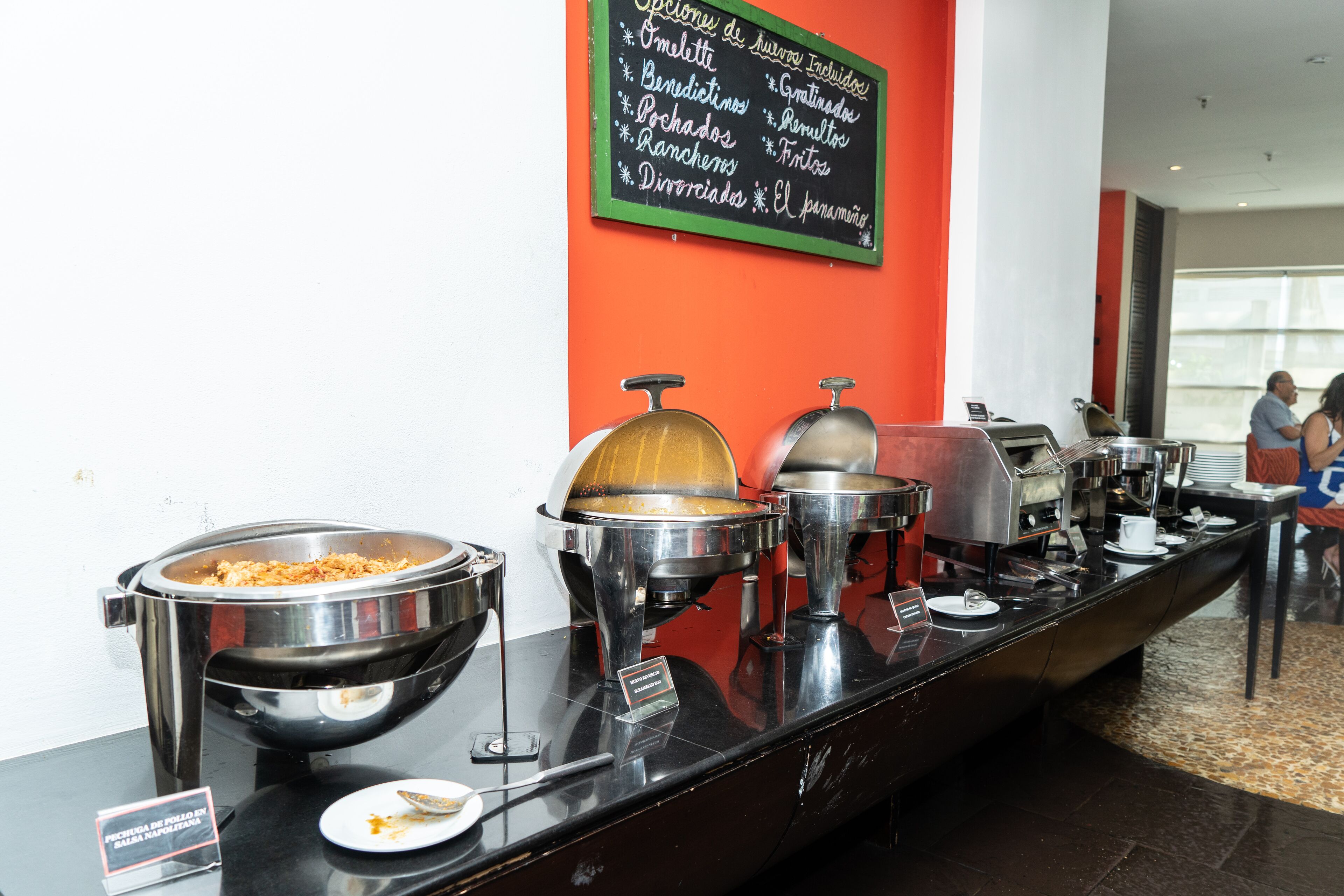 Una mesa de buffet con varios recipientes de comida y un panel de menú.