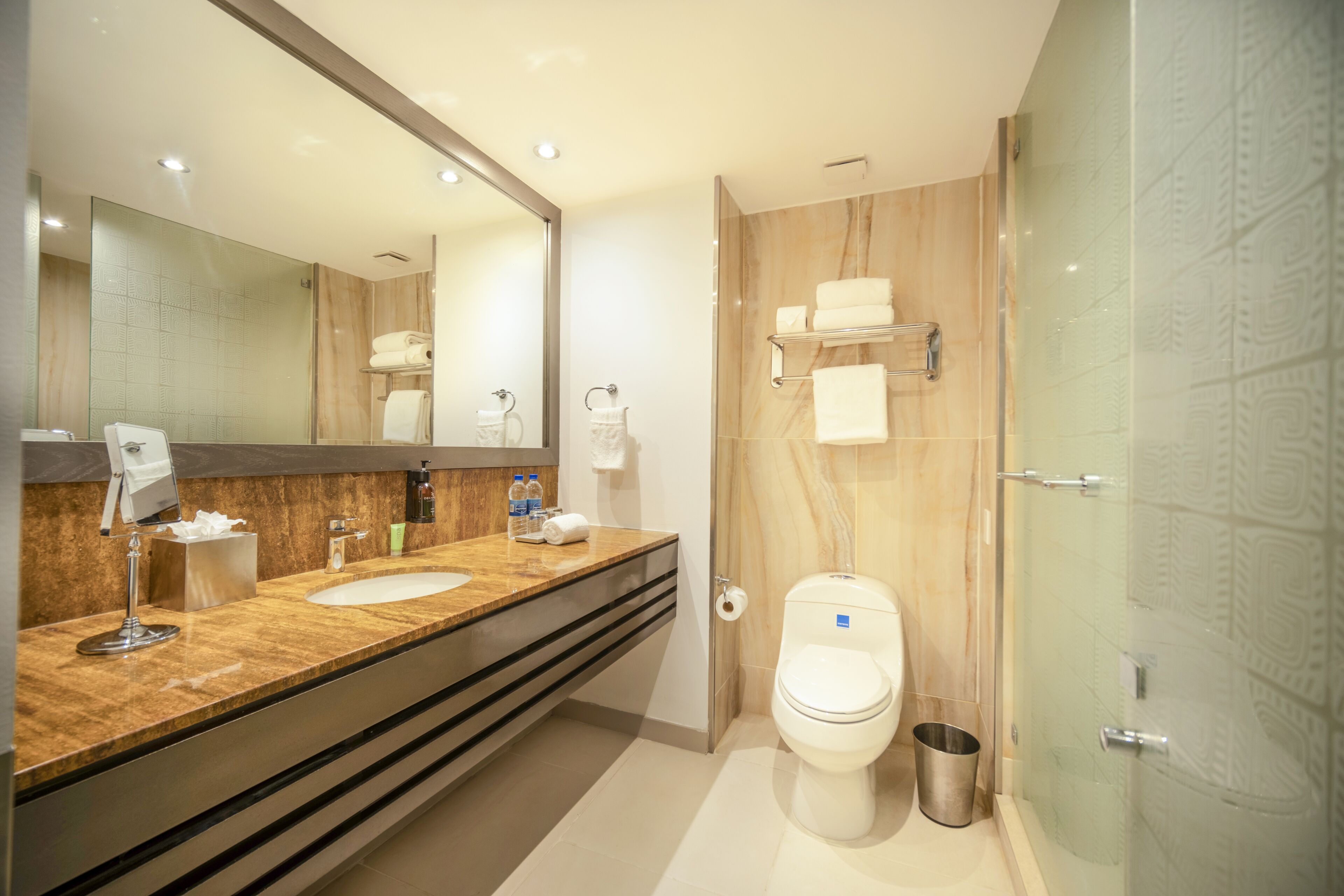 A modern bathroom with a large mirror, two sinks, a toilet, and a glass shower enclosure.