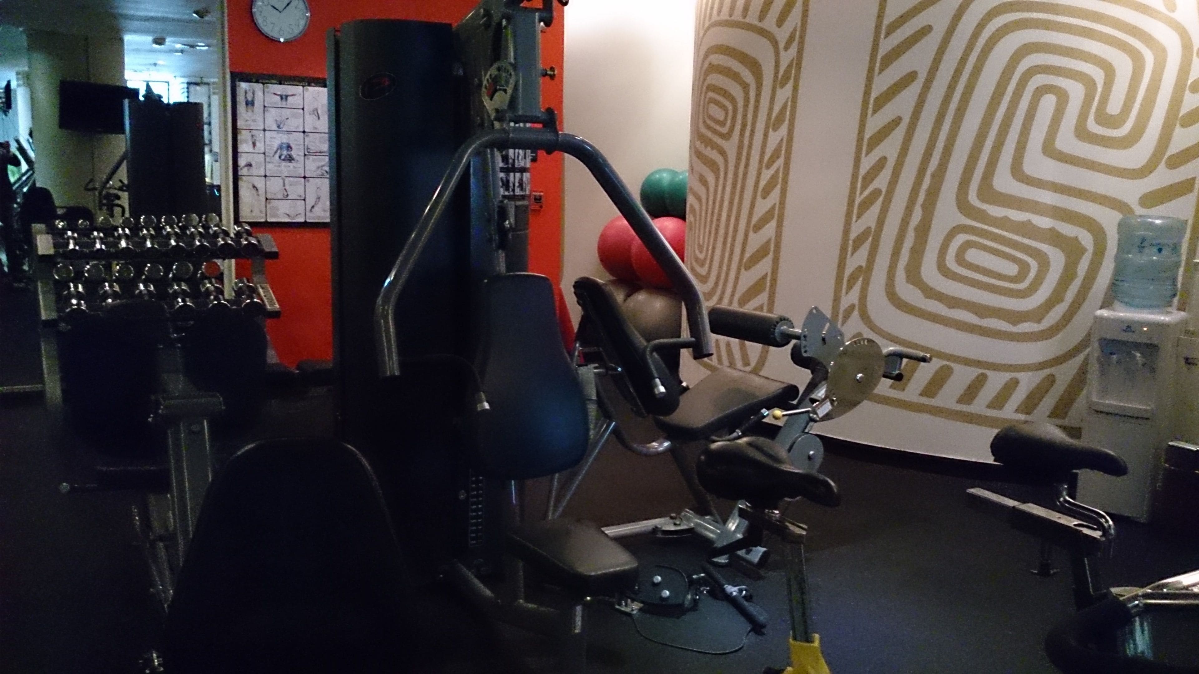 Een sportschool met fitnessapparatuur, een klok en een behang met patroon.