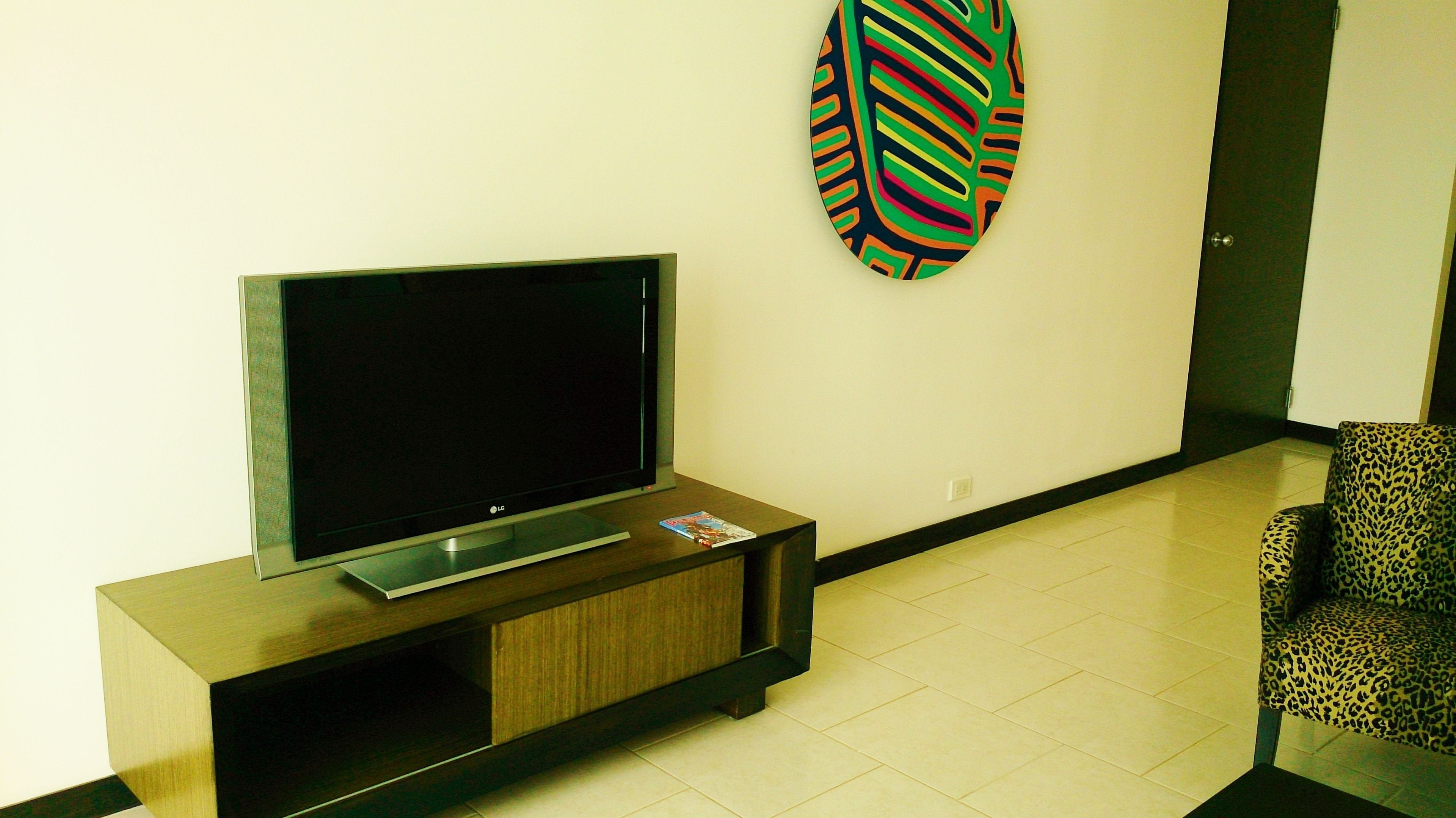 Una sala de estar moderna con un televisor de pantalla plana sobre un soporte de madera, un cuadro abstracto y colorido en la pared, y un sillón estampado de leopardo.