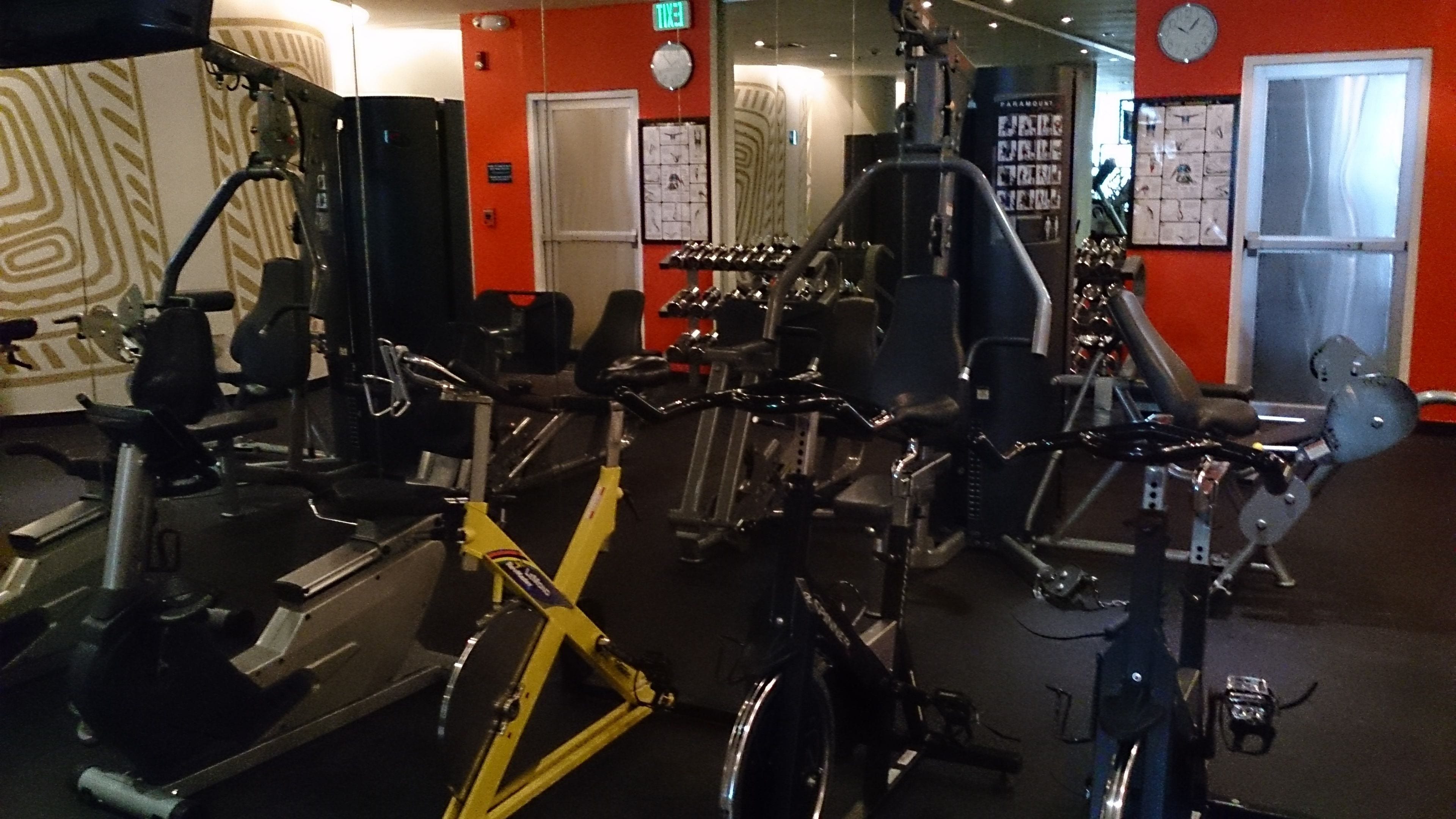 A gym with various exercise machines, including a yellow bike, and a red wall with a clock.