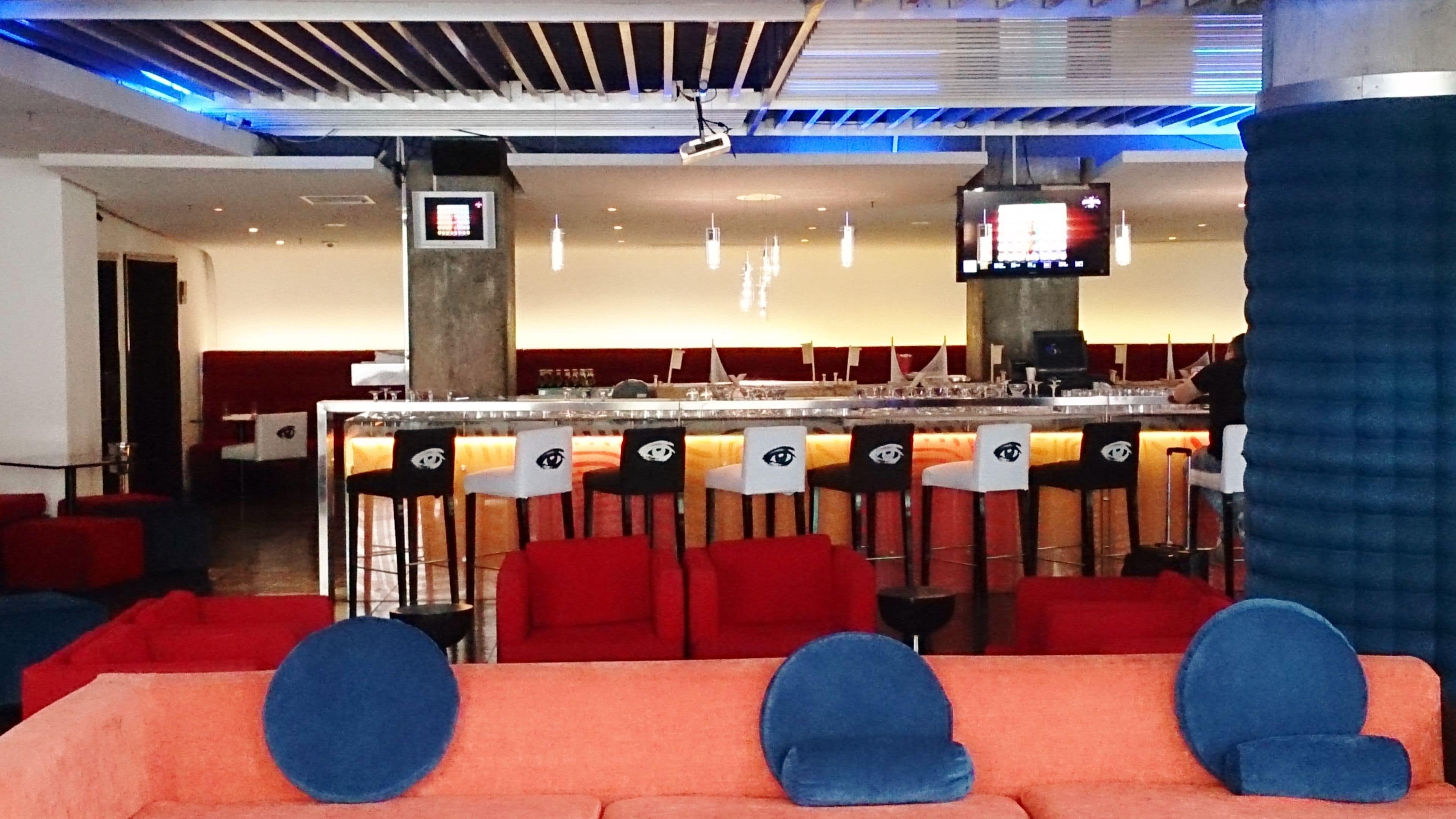 A bar area with red and black bar stools, a counter, and a television screen.