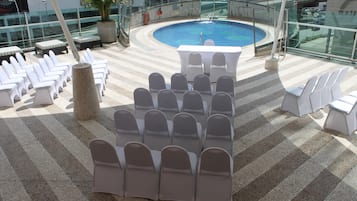 Un espace piscine aménagé sur le toit, avec des chaises longues blanches disposées en rangées, une table centrale et une rambarde en verre donnant sur la piscine.