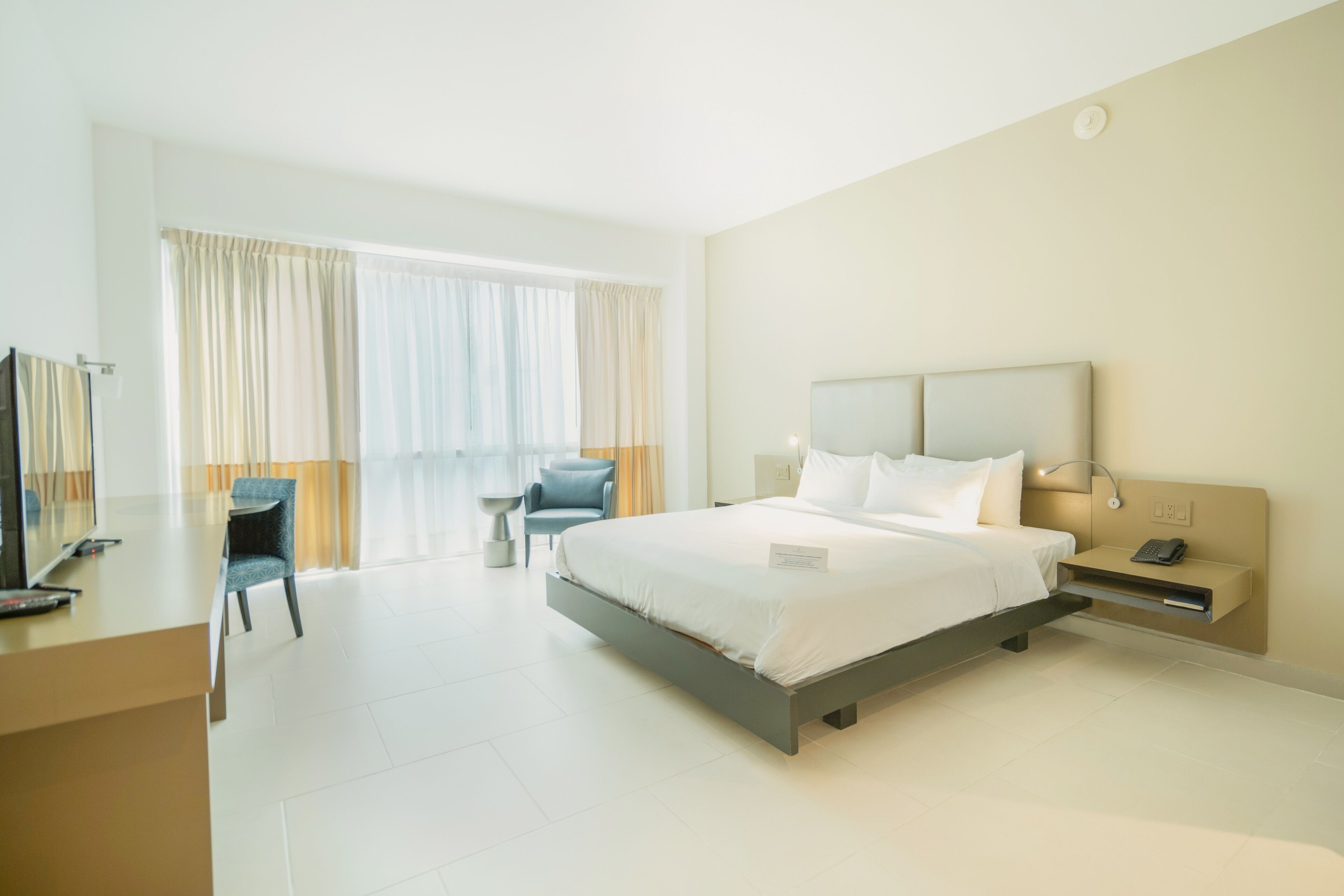 A modern hotel room with a large bed, a desk, a chair, and a small table.