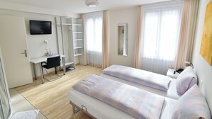 Une chambre d’hôtel avec deux lits, un bureau avec une chaise, un téléviseur fixé au mur et une salle de bain visible à travers une porte.
