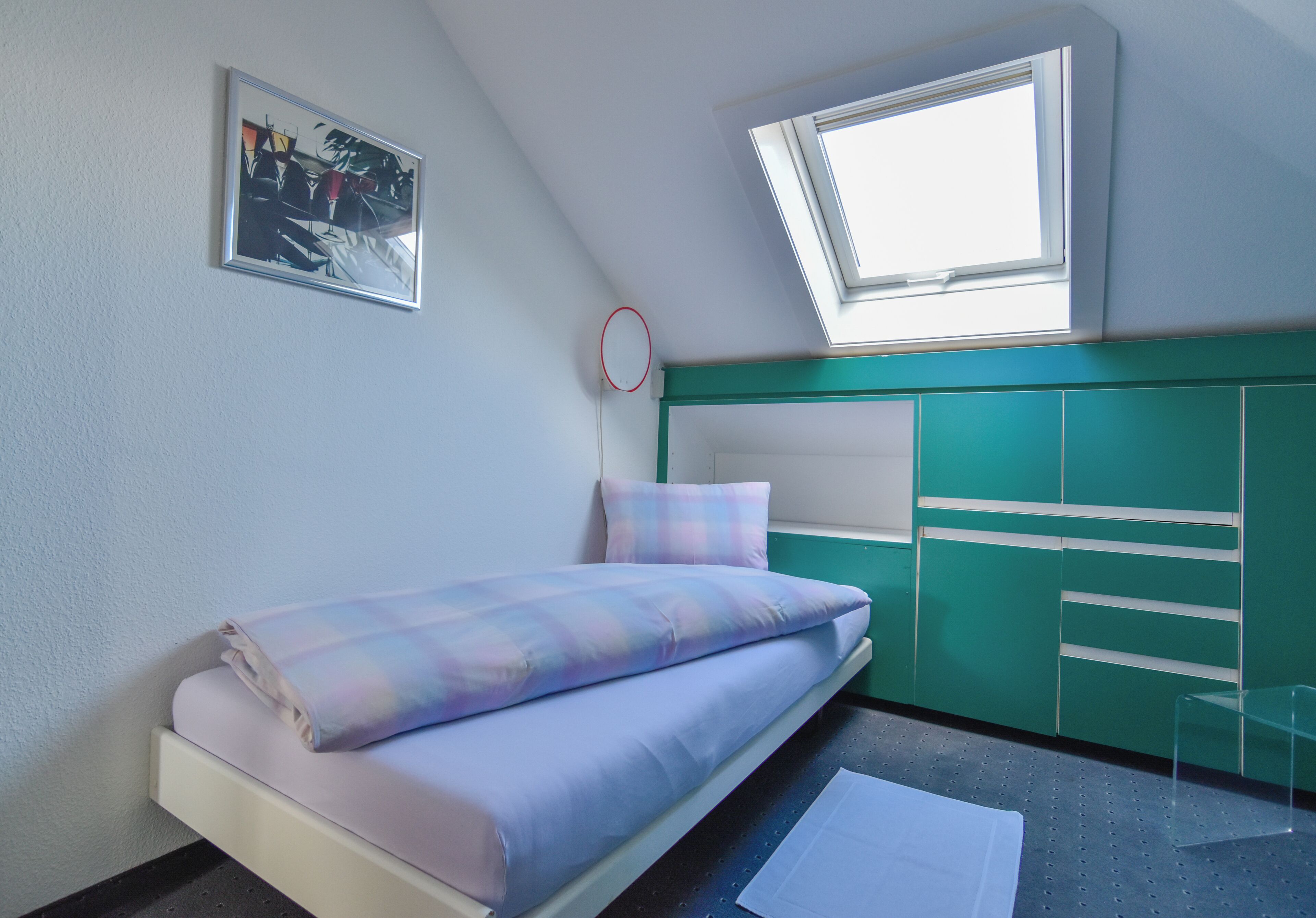 A bedroom with a bed, a window, a green cabinet, and a framed picture on the wall.
