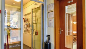 L’entrée d’un hôtel, avec un comptoir d’accueil, une porte en bois et une porte vitrée donnant sur le hall d’entrée.