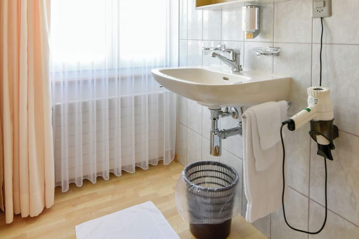 Ein Badezimmer mit Holzboden, einem weißen Waschbecken, einem Spiegel und einem Fenster mit durchsichtigen Vorhängen.
