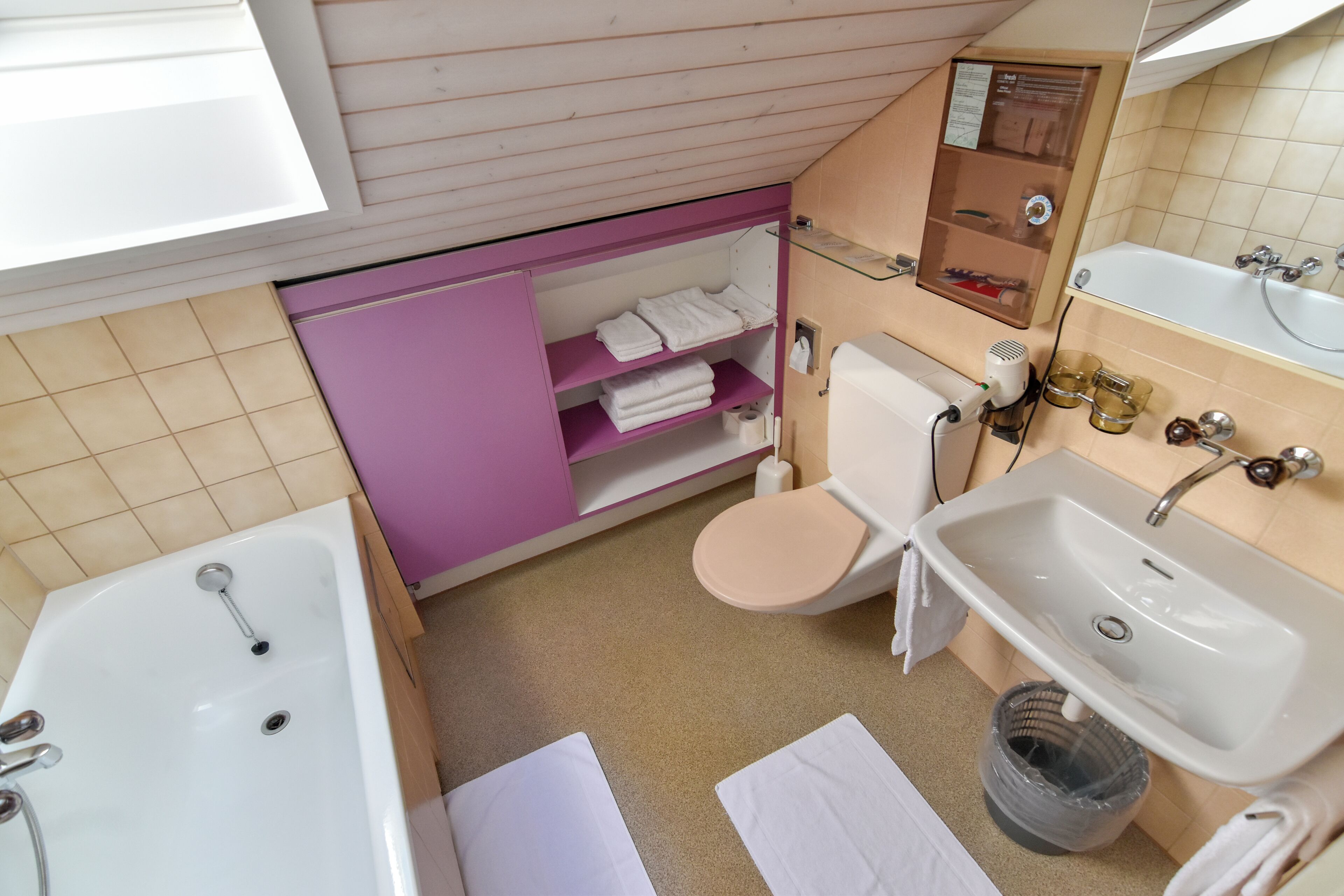 A bathroom with a bathtub, toilet, sink, and a shelf with towels.