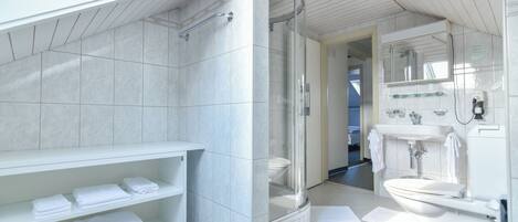 A modern bathroom with a glass-enclosed shower, white tiles, a vanity with a mirror, and neatly folded towels on shelves.