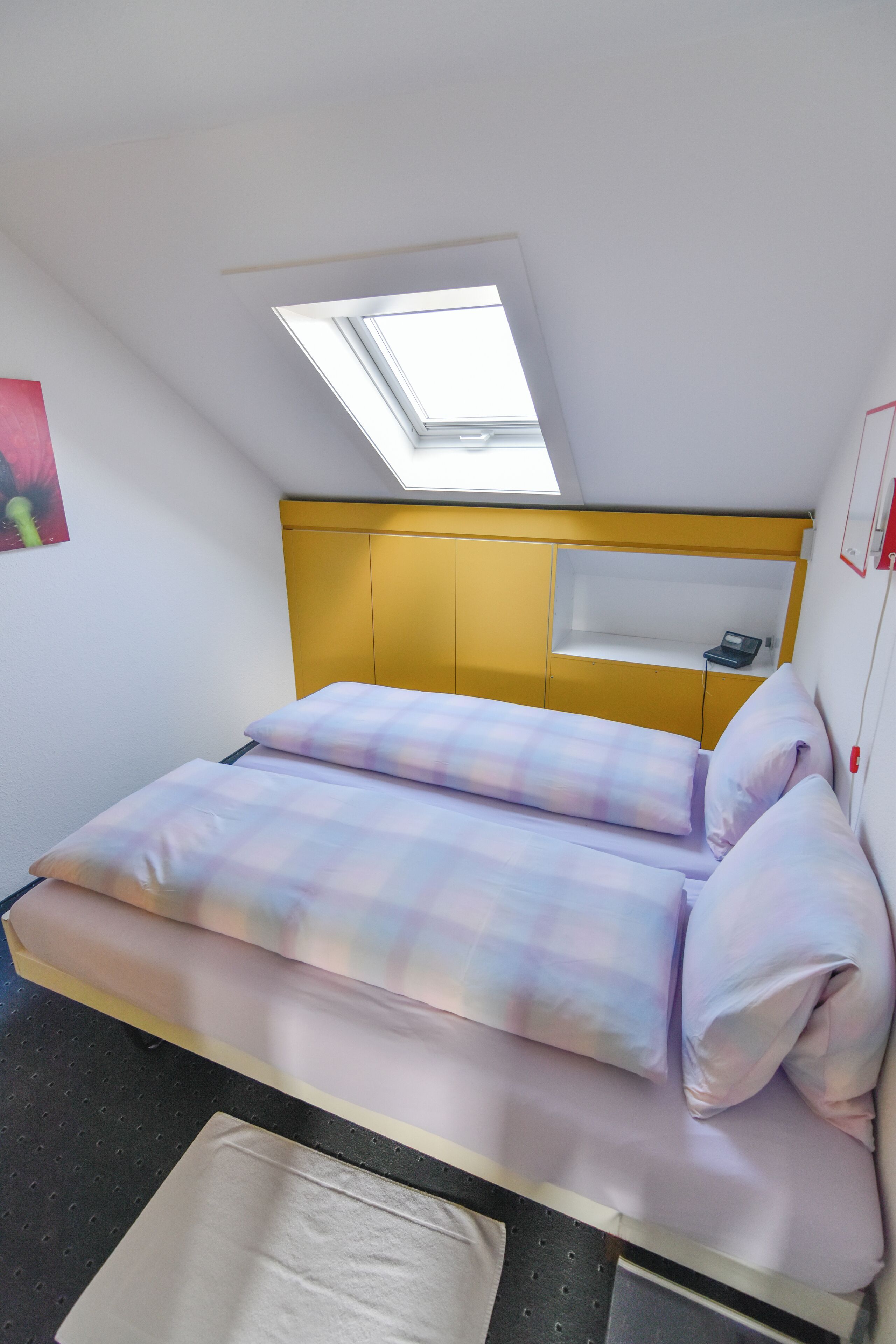A bedroom with a bed, a skylight, and a yellow headboard.