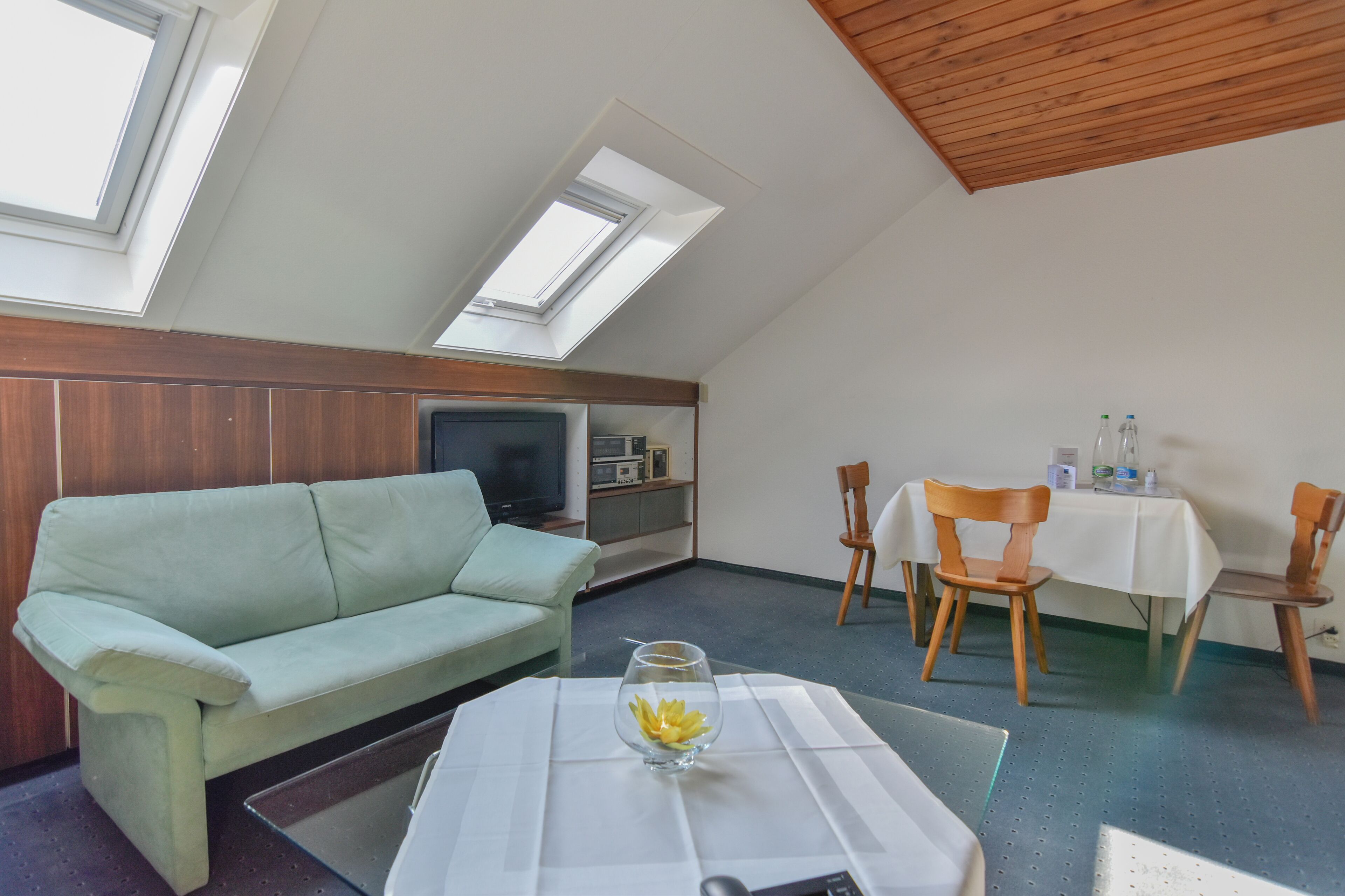 Una habitación con sofá, una mesa con un florero de vidrio, televisor y un área de comedor con sillas y mesa.