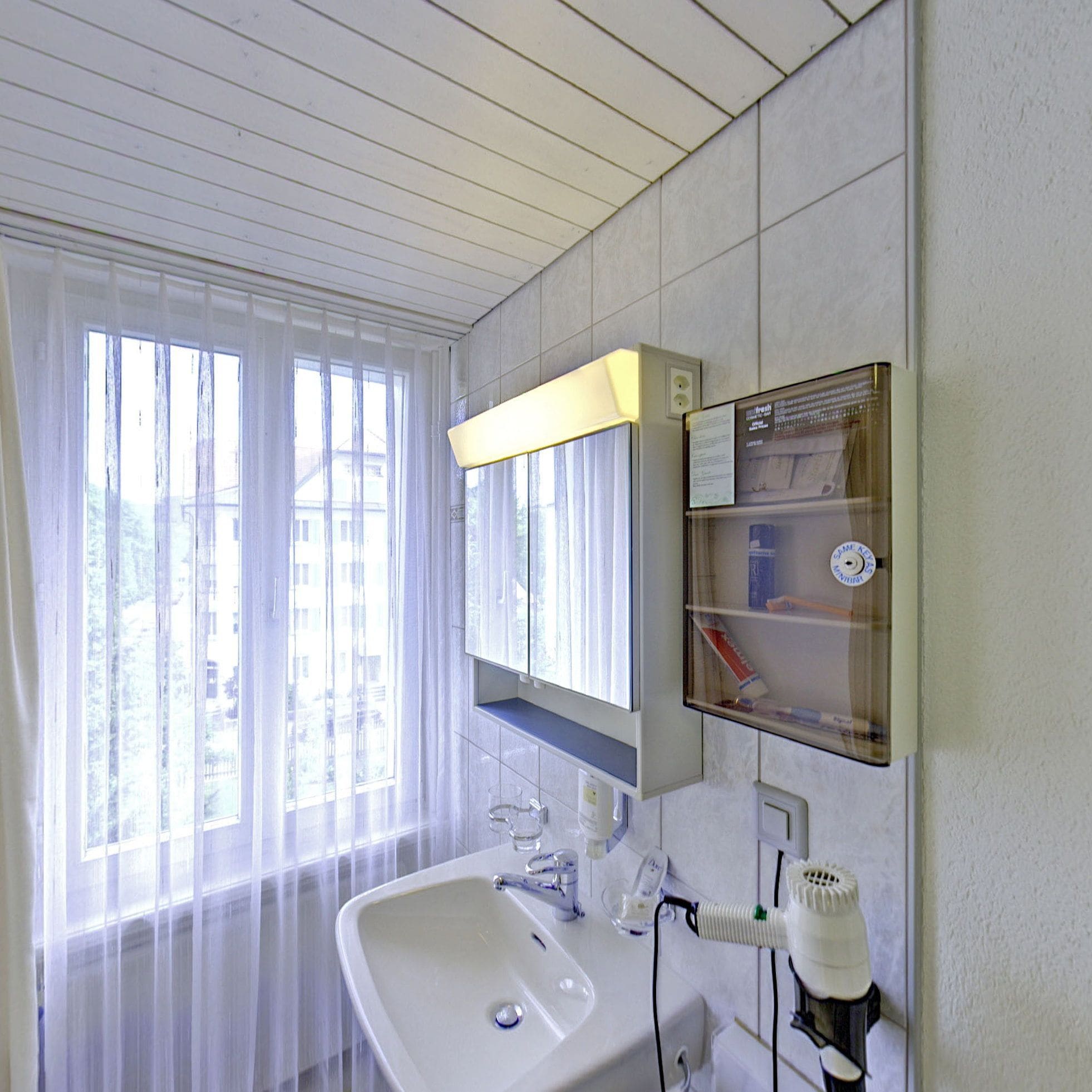 A bathroom with a large window, a sink, a mirror, and a shelf with toiletries.