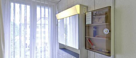 A bathroom with a large window, a sink, a mirror, and a shelf with toiletries.