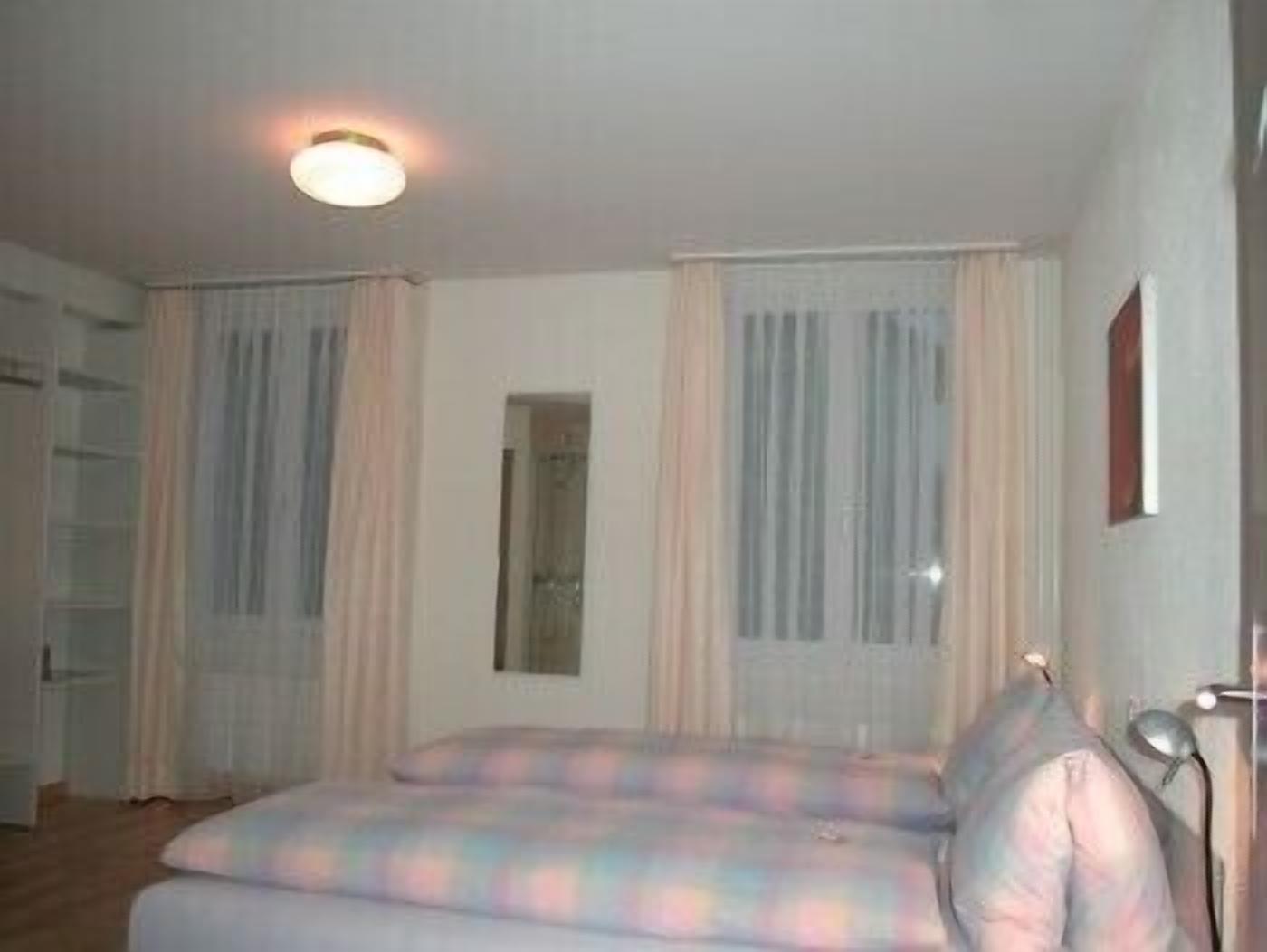 A bedroom with a bed, a bedside table, a lamp, and a window with curtains.