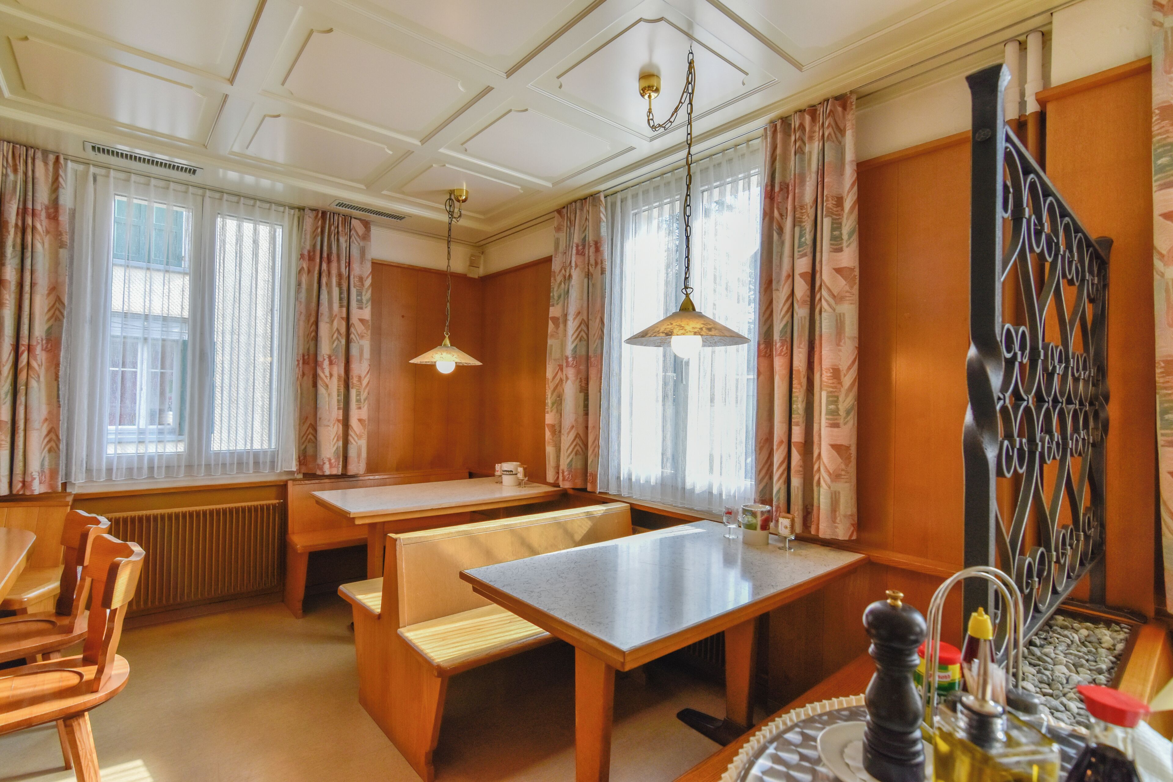 Een eetruimte met houten meubels, een tafel, bankjes en een decoratieve metalen scheidingswand.