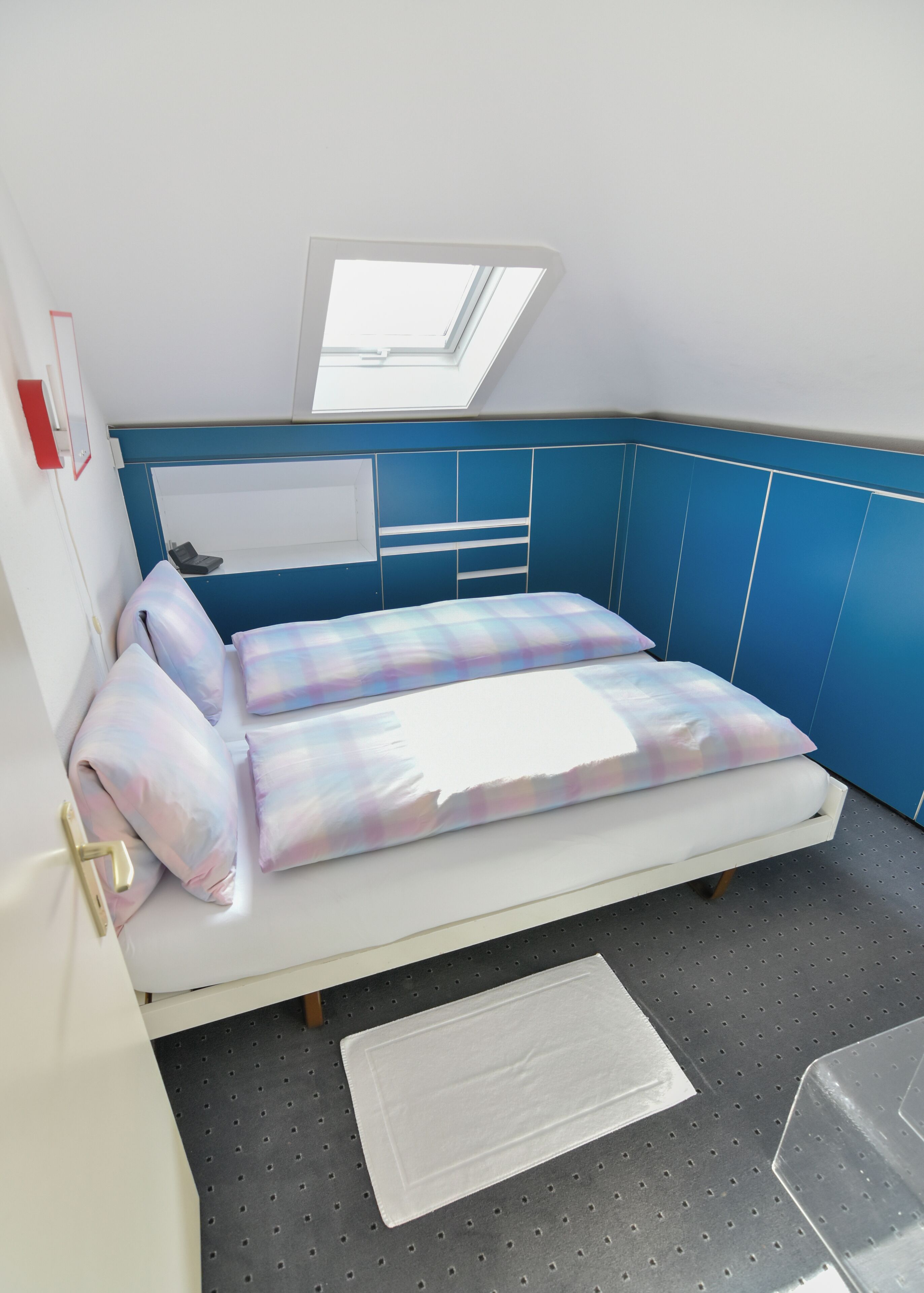 A small, compact bedroom with a bunk bed, a skylight, and a small desk area.