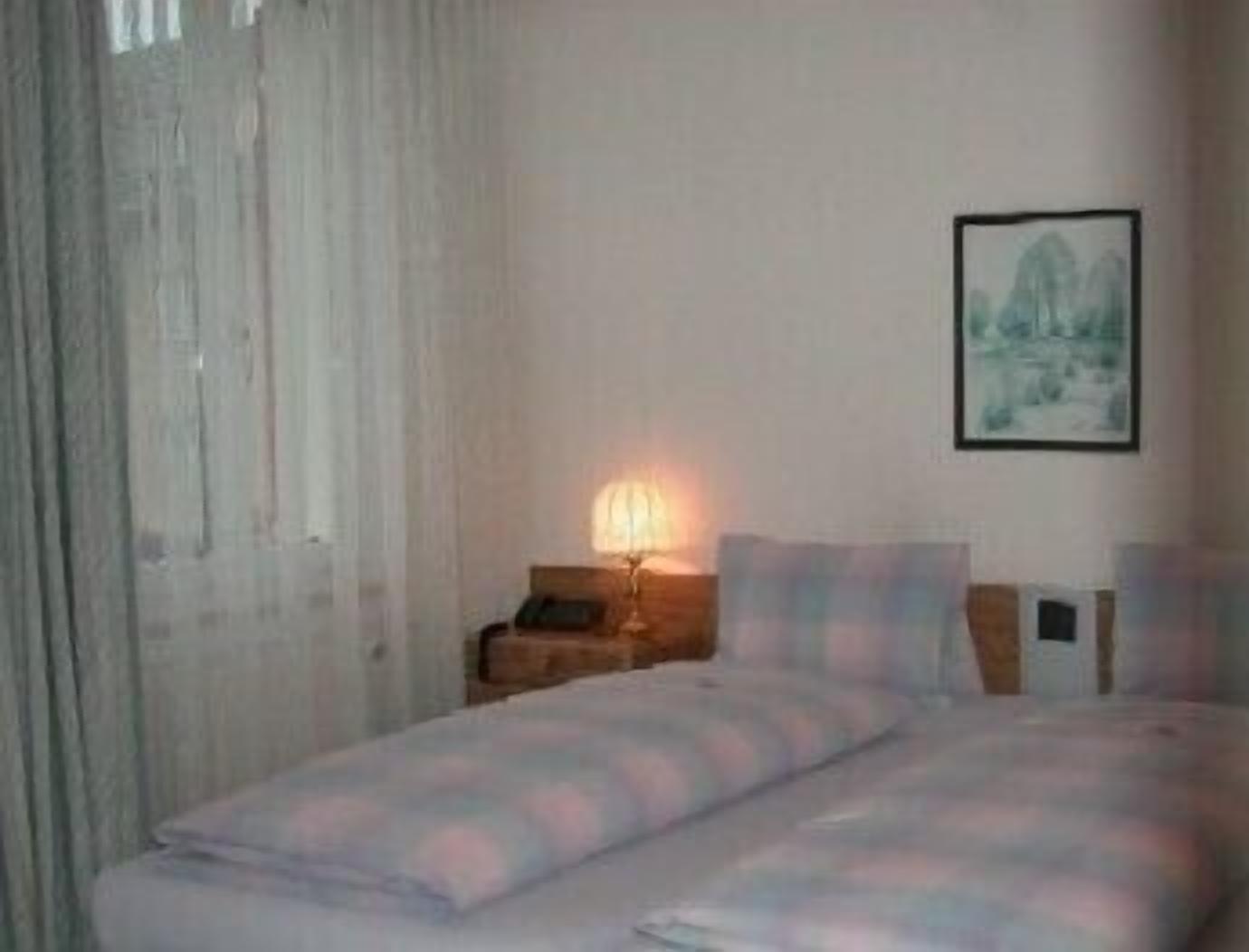 A hotel room with a bed, a nightstand, a lamp, and a framed picture on the wall.