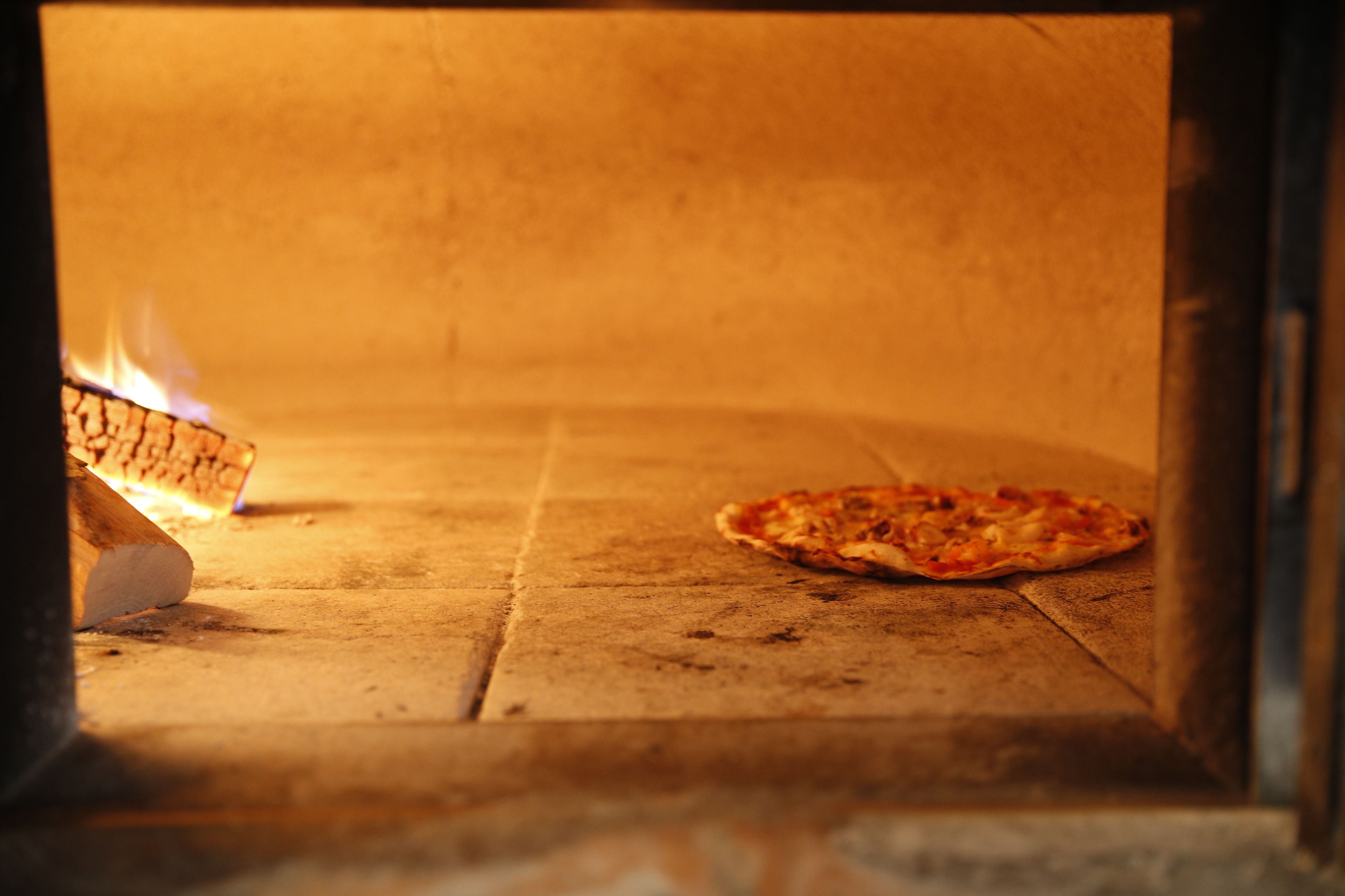 A pizza inside a wood-fired oven with a fire burning on one side.