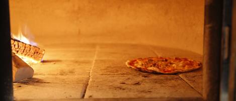 A pizza inside a wood-fired oven with a fire burning on one side.