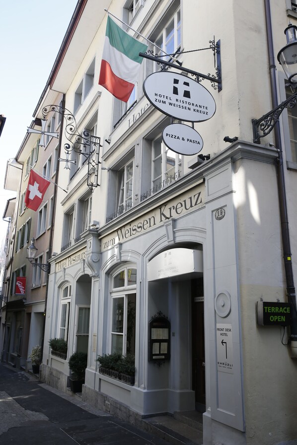 Un hôtel appelé « Zum Weissen Kreuz », avec une enseigne indiquant « Hôtel-restaurant Zum Weissen Kreuz » et « Pizza et pâtes ».