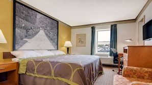 Une chambre d’hôtel avec un grand lit, un bureau, une chaise, une télévision et une fenêtre avec des rideaux.