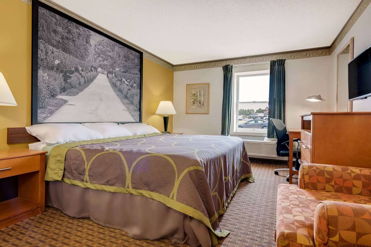 Une chambre d’hôtel avec un grand lit, un bureau, une chaise, une télévision et une fenêtre avec des rideaux.