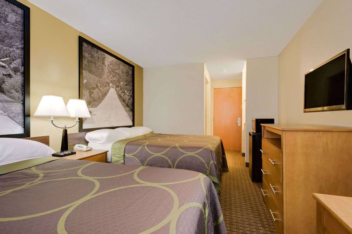 Une chambre d’hôtel avec deux lits, un bureau avec une lampe, une télévision et une porte donnant sur une autre pièce.
