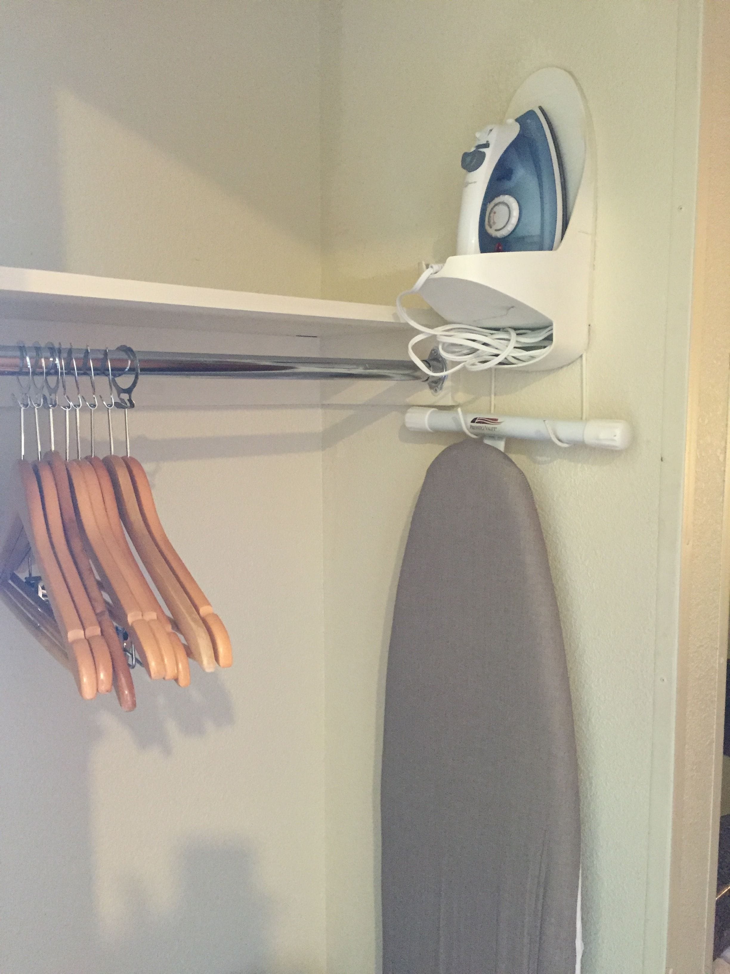 Tabla de planchar fijada a la pared, con un planchador y un perchero.