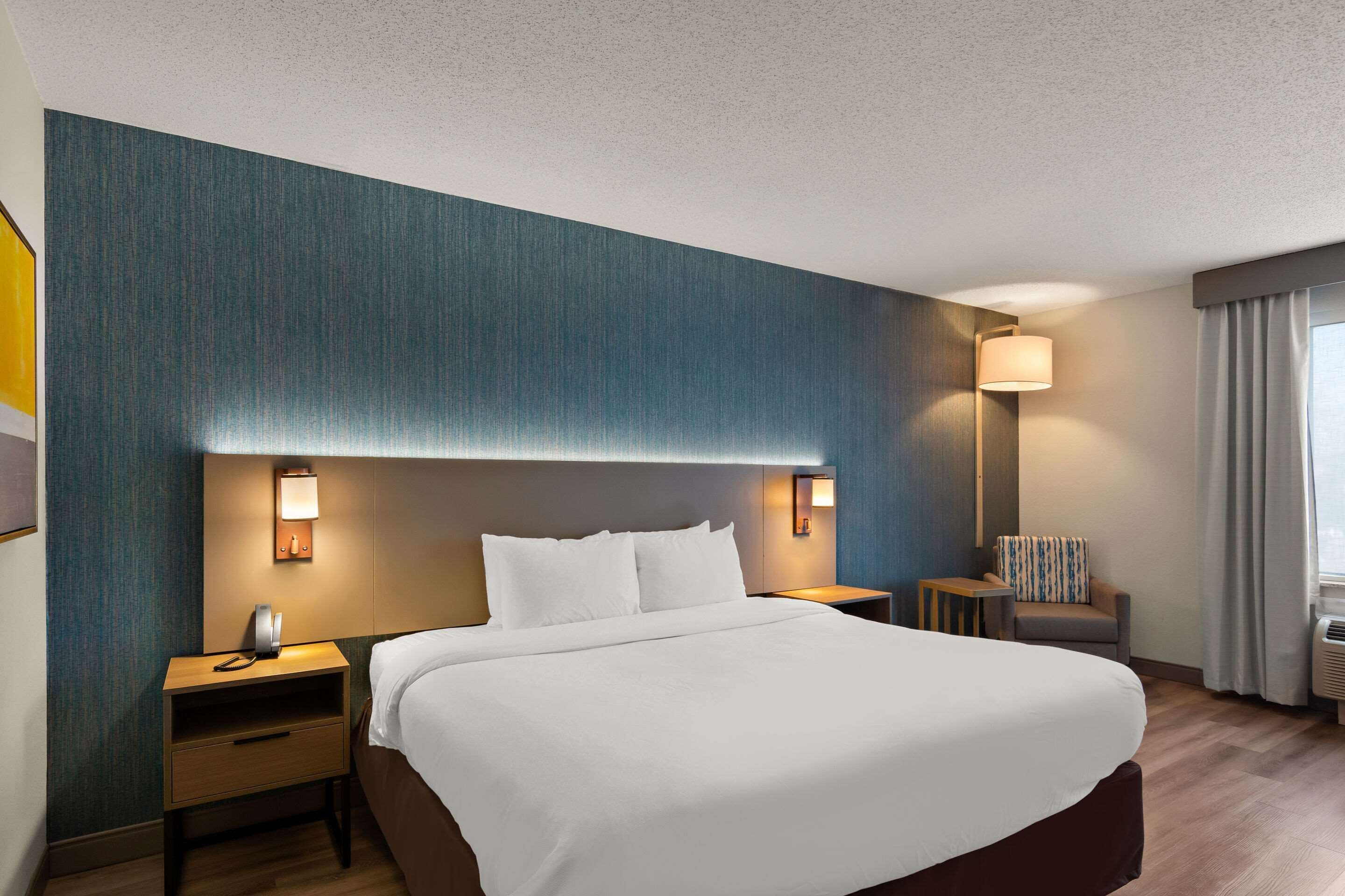 Ein Hotelzimmer mit einem großen Bett, Nachttischen, einer Lampe, einem Sessel und einem Fenster mit Vorhängen.