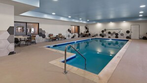 Piscina interna com parede de azulejos hexagonais, escada para piscina e área de estar com mesas e cadeiras.