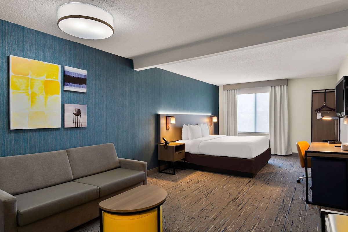 Ett modernt hotellrum med en säng, en soffa, ett skrivbord och en TV.