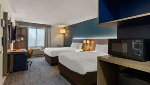 Quarto de hotel com duas camas, uma escrivaninha com computador, micro-ondas e televisão.