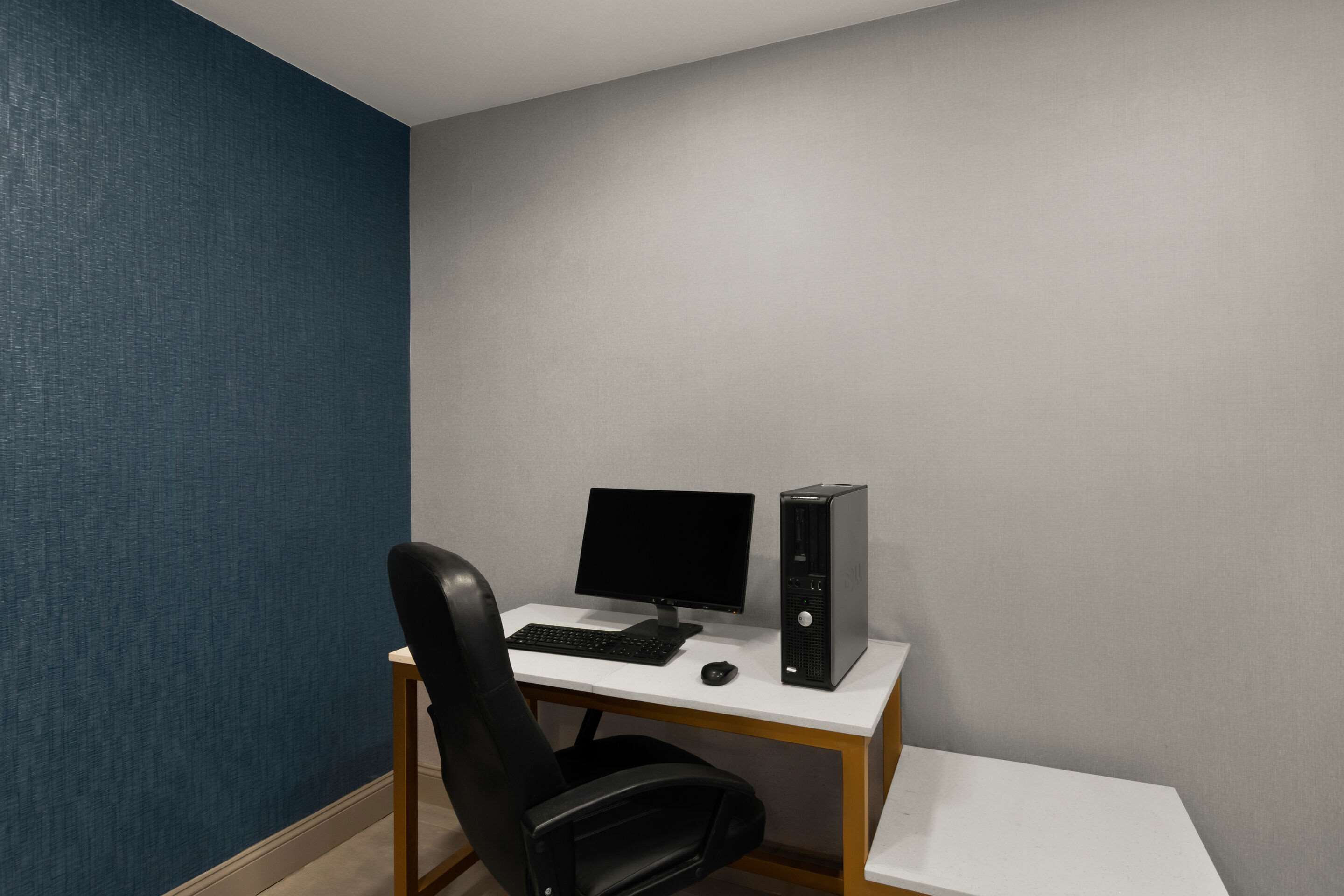 A computer desk with a monitor, keyboard, and tower PC in a room with blue and gray walls.