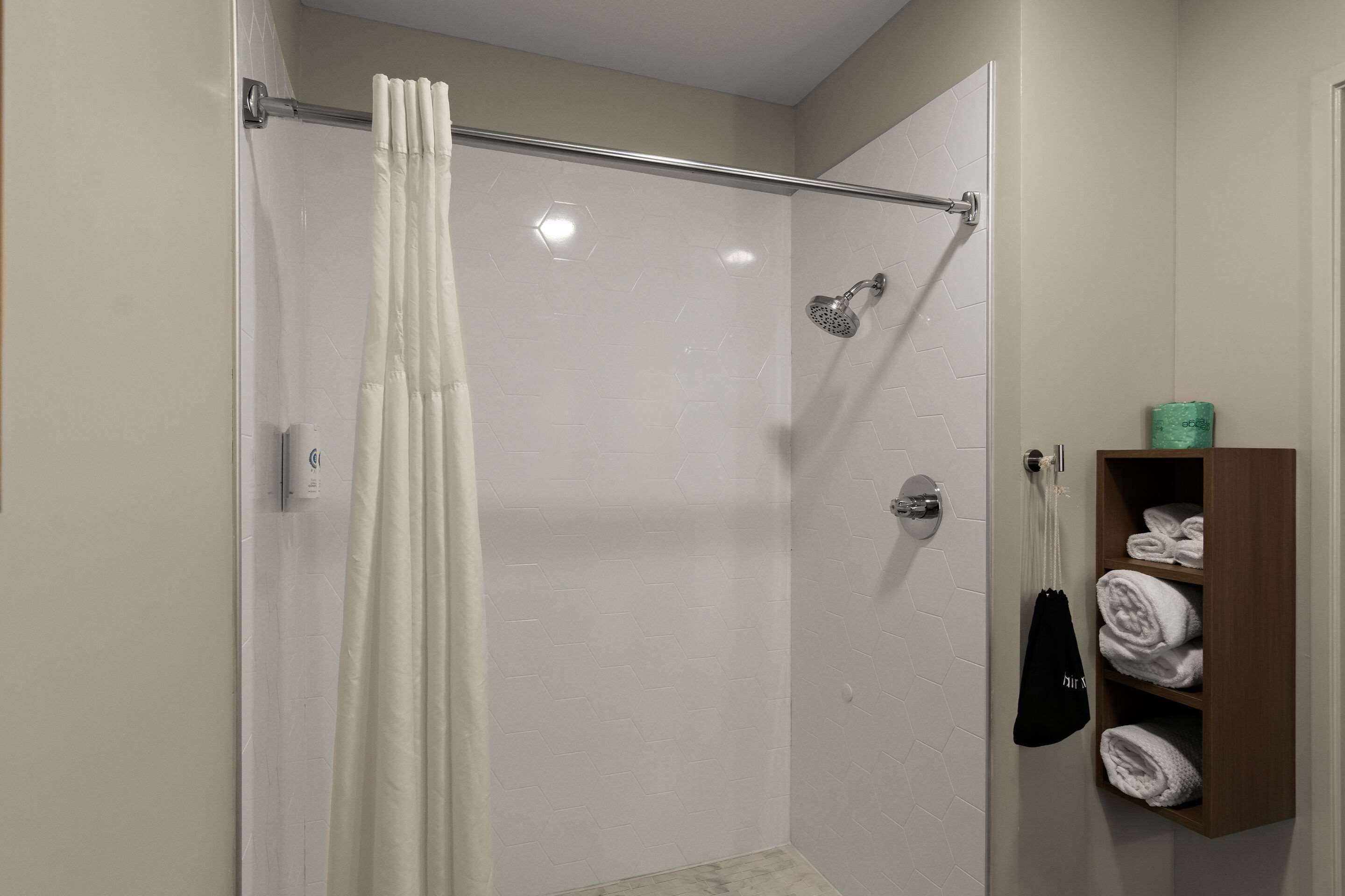 A shower with a white curtain, a handheld showerhead, and a towel rack with folded towels.