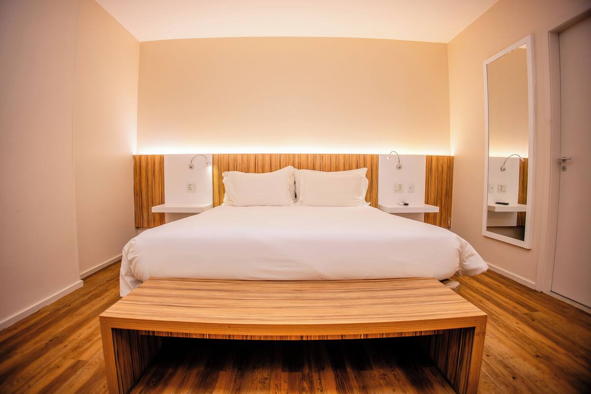 Een moderne slaapkamer met een groot bed, een houten hoofdbord, nachtkastjes en een spiegel.