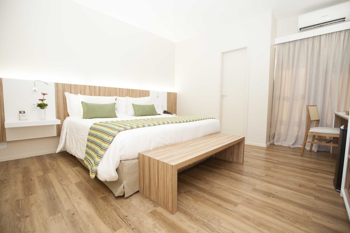 Een moderne slaapkamer met een houten bed, nachtkastje, bankje en een airconditioning.