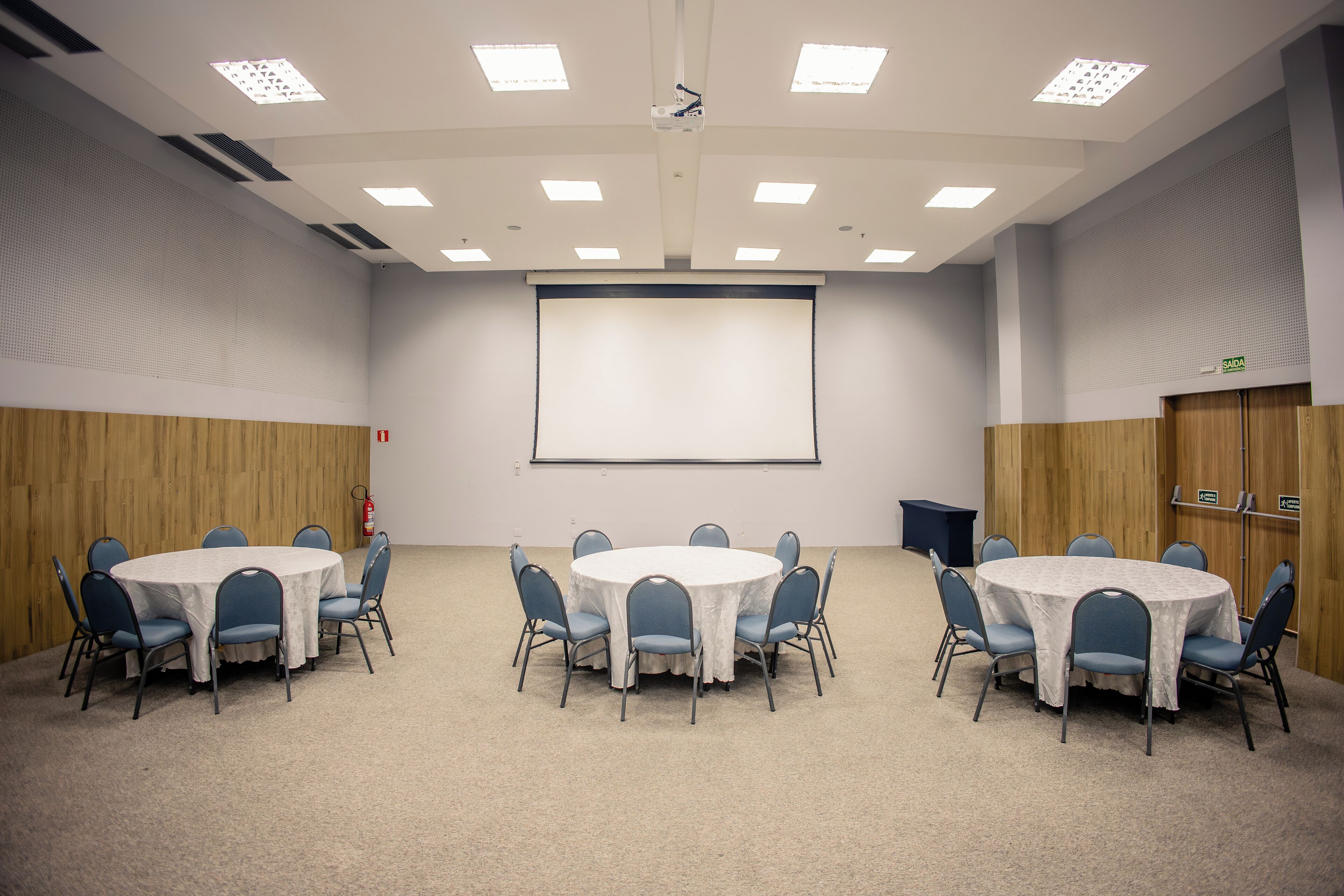 A conference room with a white table, blue chairs, a projector screen, and a whiteboard.