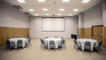 Une salle de conférence avec une table blanche, des chaises bleues, un écran de projection et un tableau blanc.